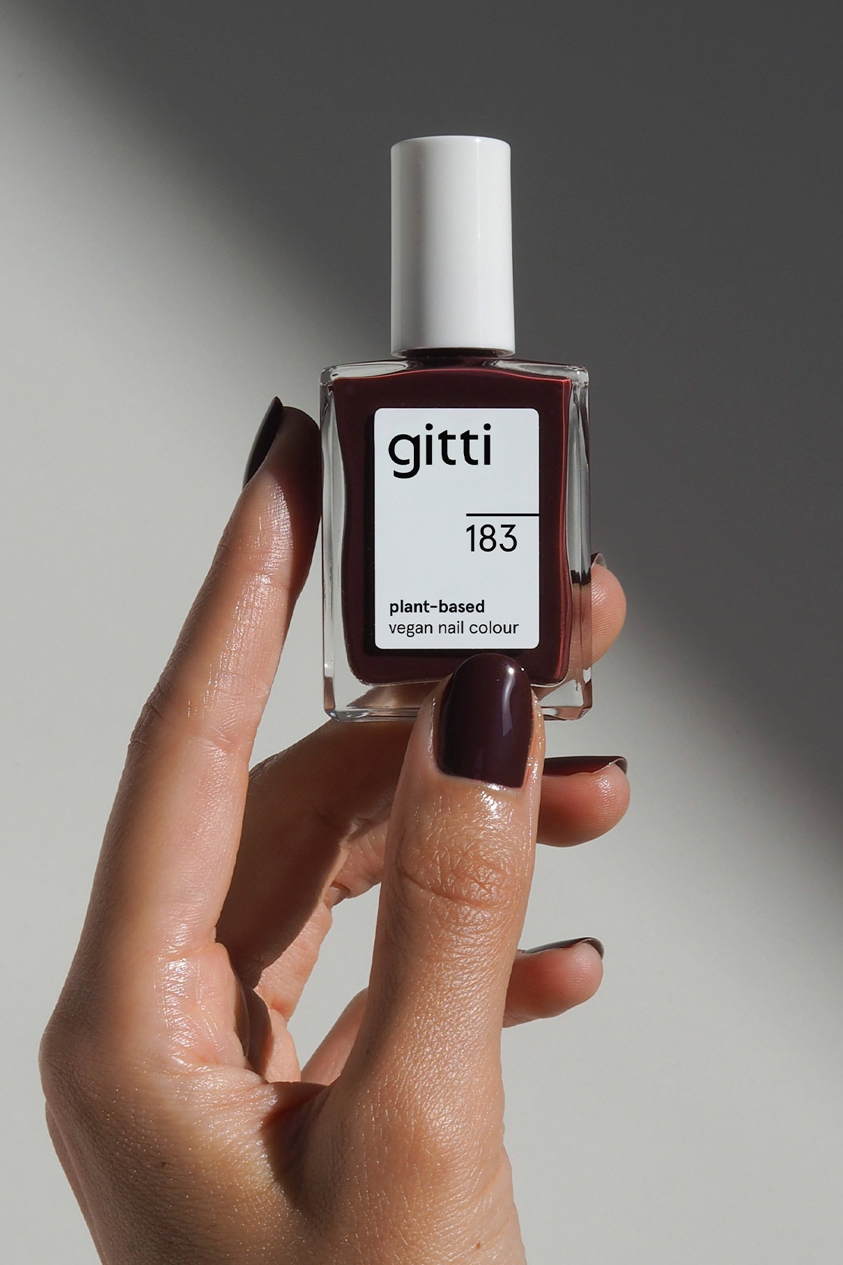 Eine Hand hält eine Flasche von gitti no. 183, einem pflanzlichen veganen Nagellack in einem intensiven Beerenrot; die Nägel sind in der gleichen dunklen beerenroten Farbe lackiert.