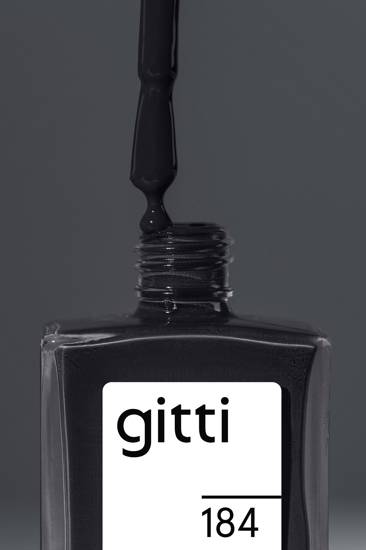 Eine Nahaufnahme einer Flasche gitti no. 184 schwarzem Nagellack in dunklem Anthrazit, mit einem Pinsel, der den satten Anthrazit-Ton in die offene Flasche tropft.