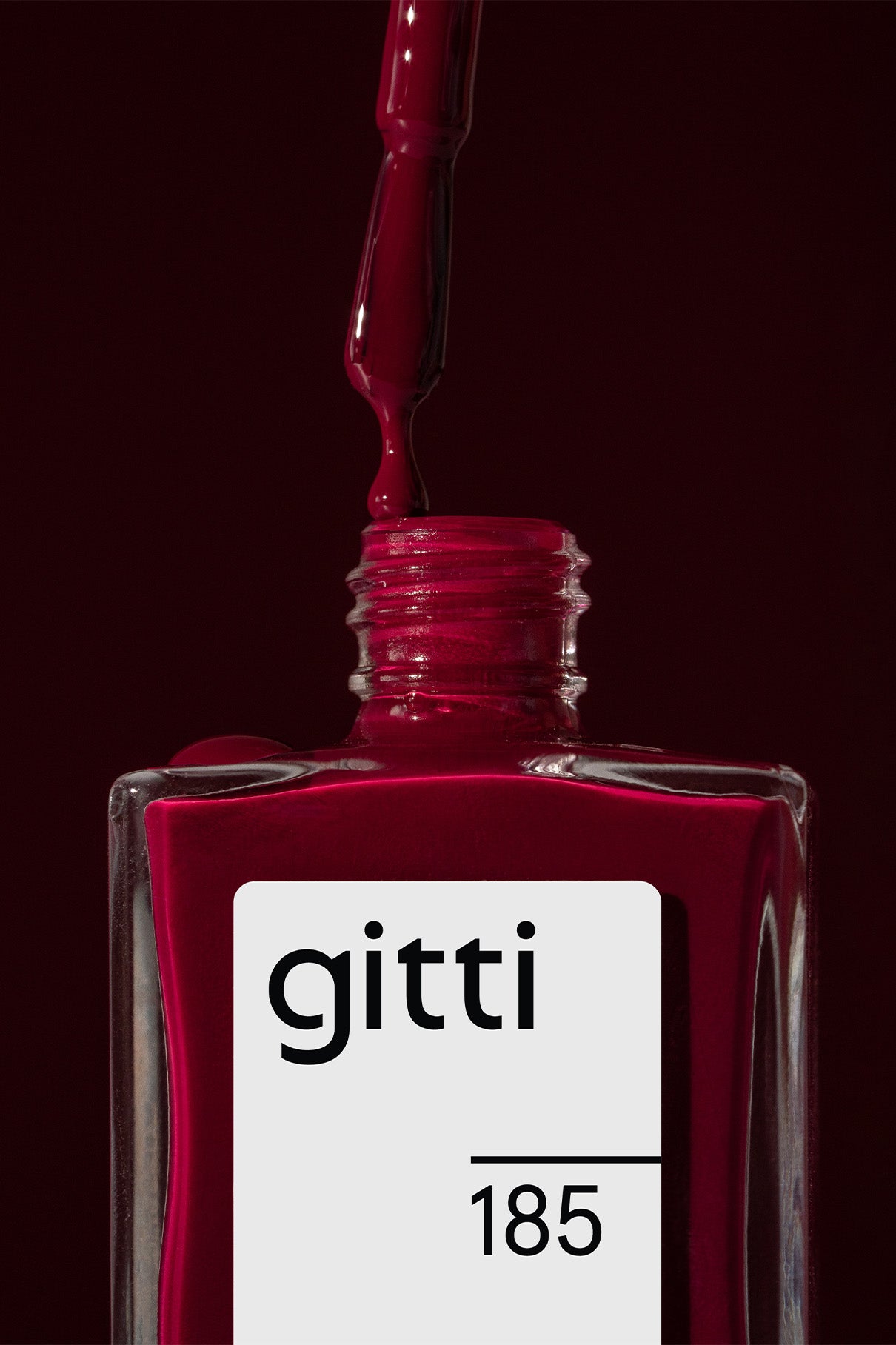 Ein Nagellackfläschchen in tiefem Rot, beschriftet mit gitti no. 185, und Pinselapplikator vor passendem Hintergrund - der perfekte kühle Rotton.