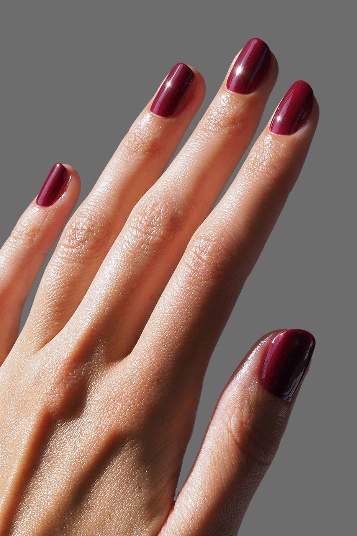Nahaufnahme einer Hand mit kurzen, sauber manikürten Nägeln, die in Gitti Nr. 185, einem tiefen Rot mit kühlen Untertönen, vor einem schlichten grauen Hintergrund.