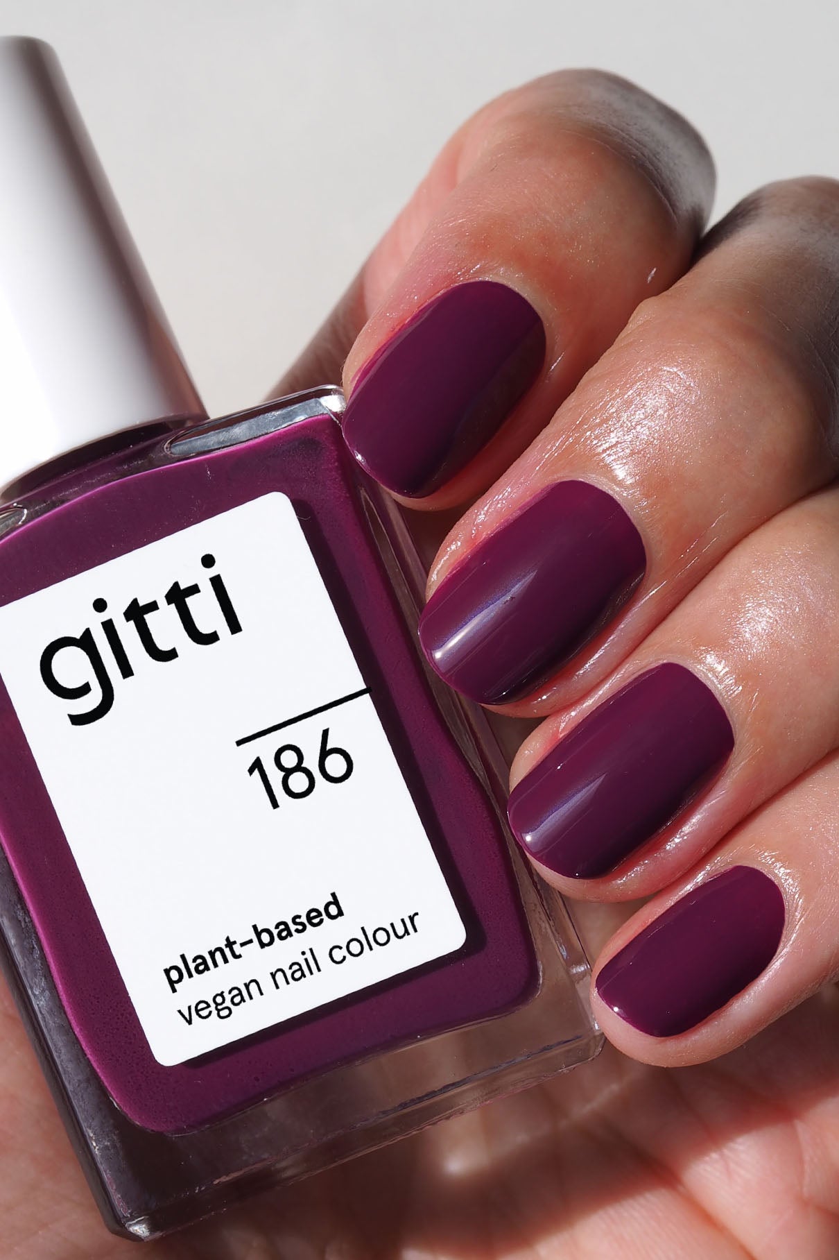 Eine Hand mit kurzen, fein säuberlich lackierten Smaragdgrün-Nägeln hält eine Flasche gitti no. 186, einer veganen Nagelfarbe auf Pflanzenbasis in einem satten, passenden Grünton.