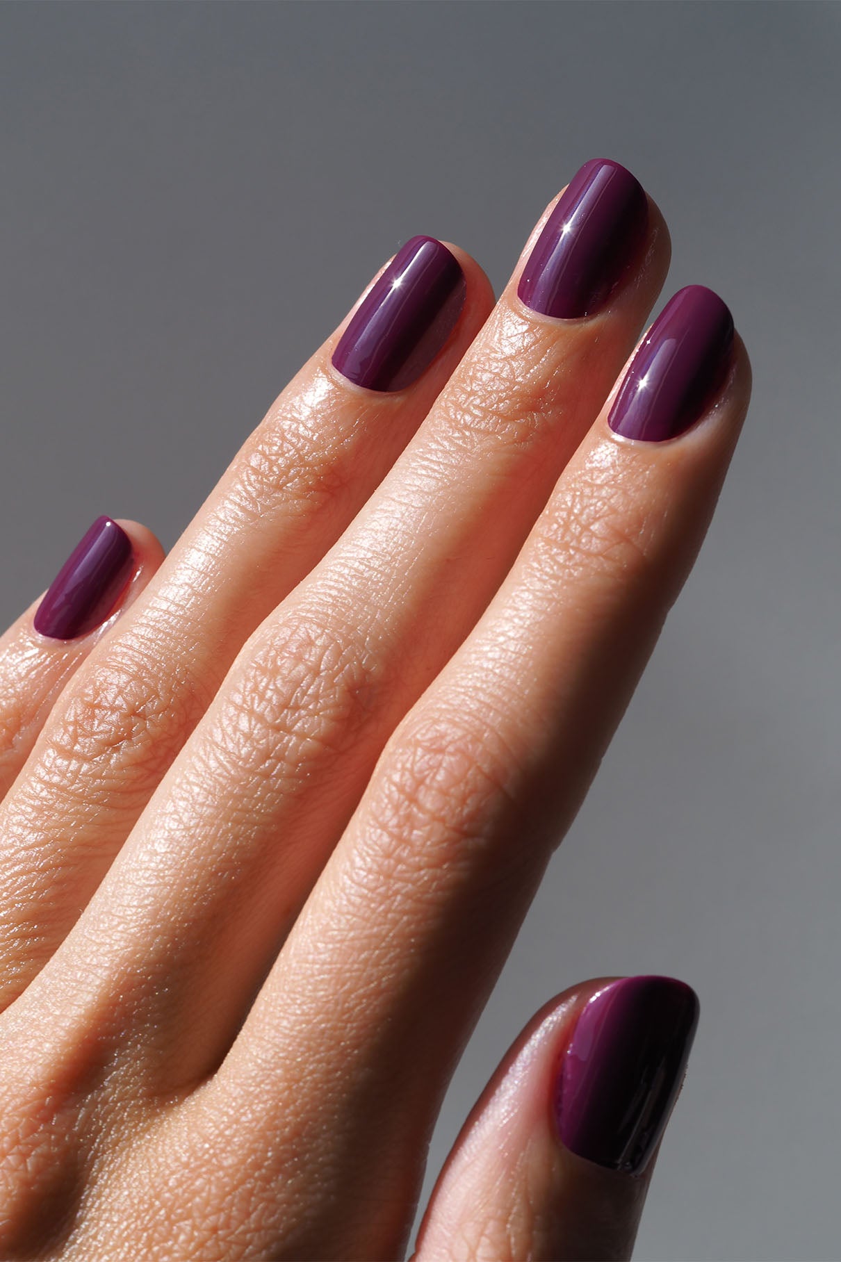 Eine Hand mit ordentlich manikürten Nägeln, die in der glänzenden dunkelvioletten Farbe gitti no. 186 und tiefgrüner Farbe.