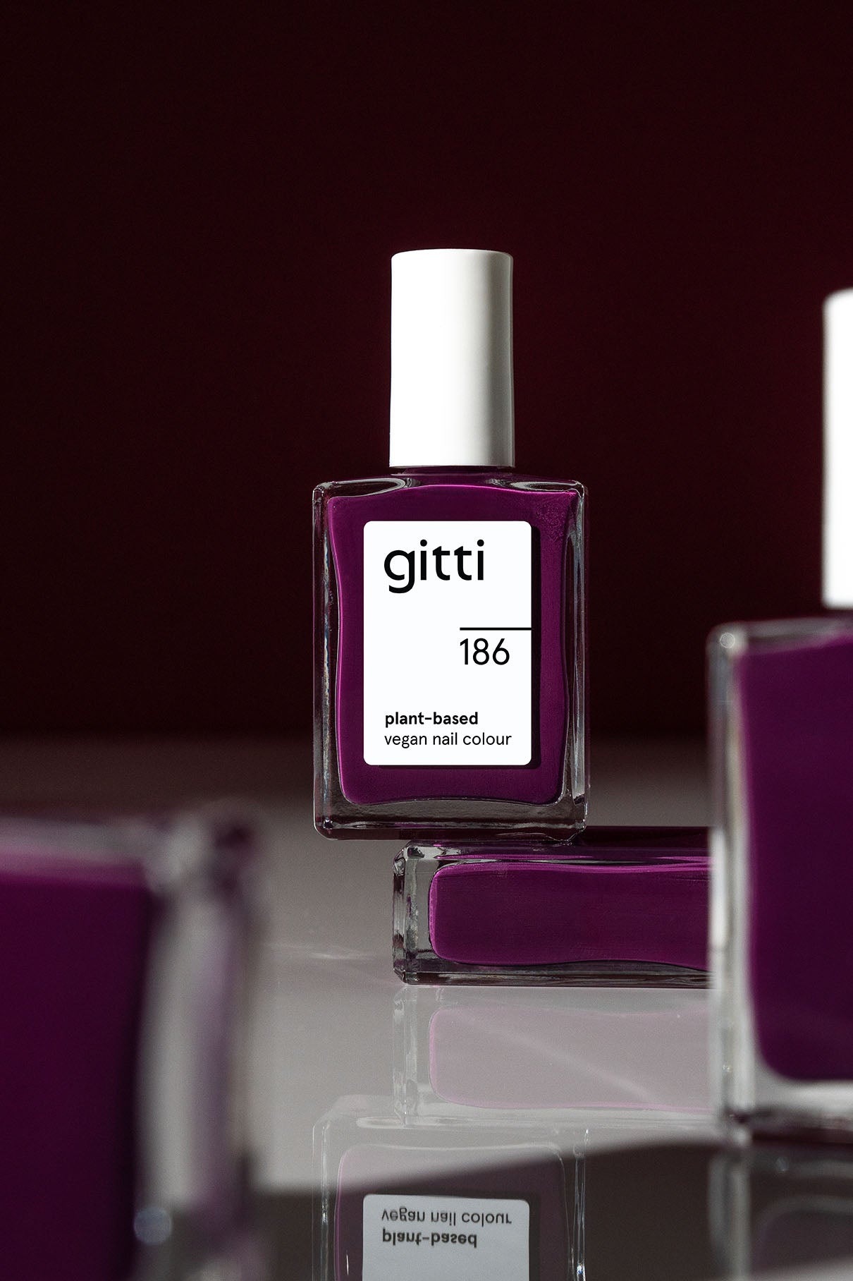 Ein Fläschchen mit gitti no. 186 pflanzliche vegane Nagelfarbe in einem tiefgrünen Farbton steht auf einer reflektierenden Oberfläche vor einem dunklen Hintergrund.