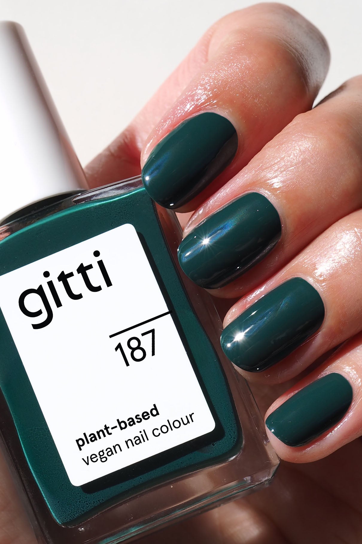 Eine Hand mit tealfarbenen Nägeln hält eine Flasche gitti no. 187, einem veganen Nagellack auf pflanzlicher Basis in einem leuchtenden Smaragdgrün, das perfekt zur Nagelfarbe passt.