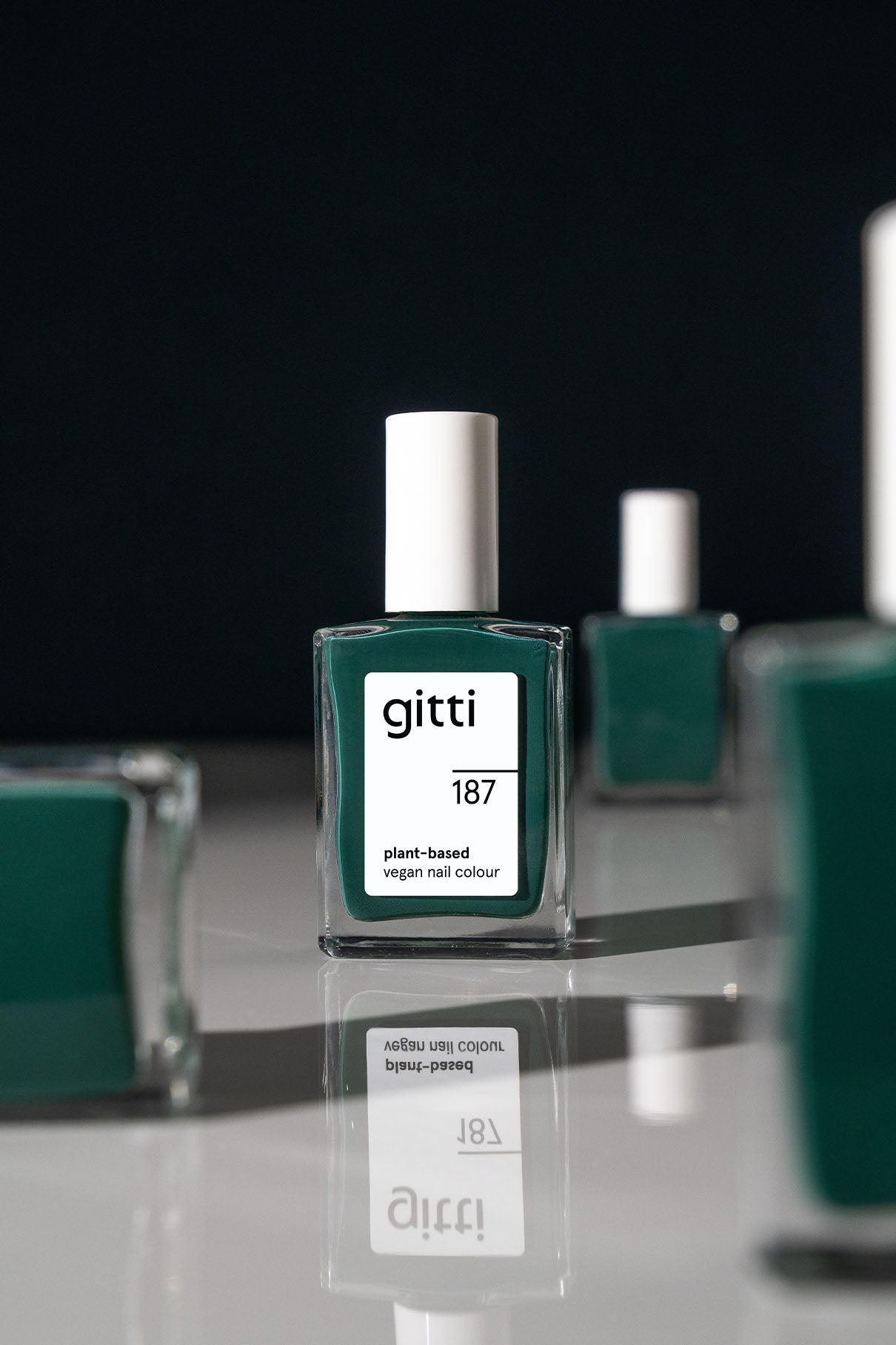 Ein Fläschchen von gitti no. 187 pflanzliche vegane Nagelfarbe in intensivem Smaragdgrün sticht hervor, während andere ähnliche Flaschen im Hintergrund verschwimmen.