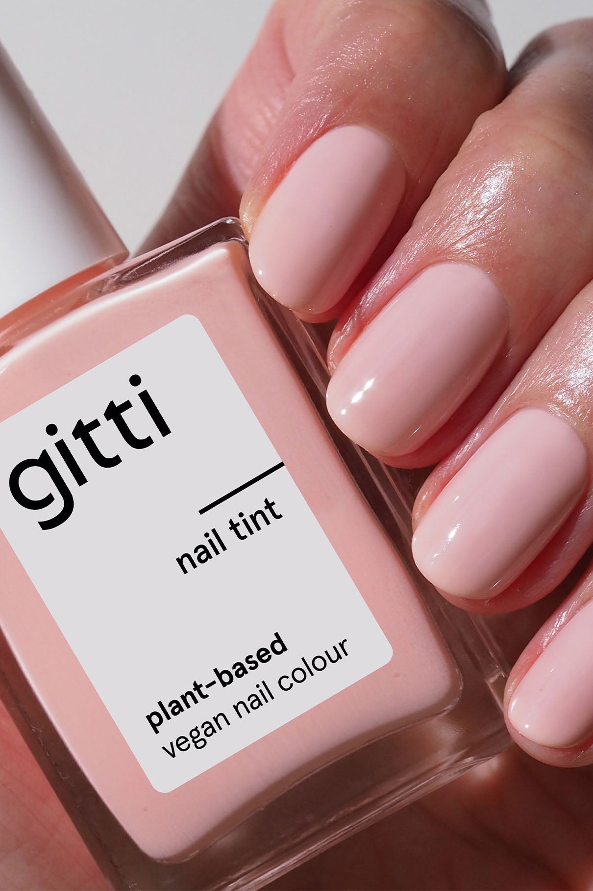 Eine Hand mit kurzen, blassrosa Nägeln hält eine Flasche mit der Aufschrift gitti nail tint - jetzt erhältlich als Community Box, ein pflanzliches, veganes Nagelfarbset mit kostenlosem Versand.