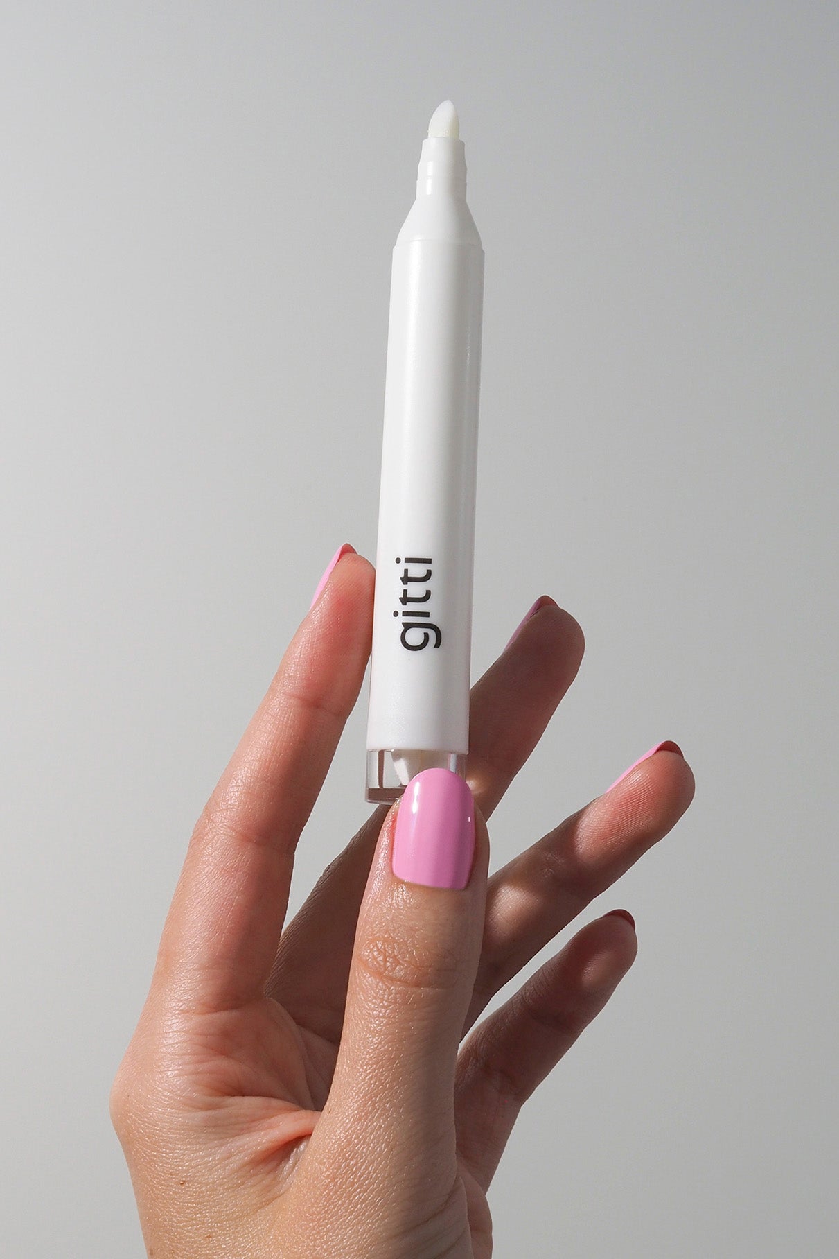Eine Hand mit rosafarbenen Nägeln hält den weißen gitti Corrector Pen aus dem Set Plant Duo + Corrector Pen vor einem hellen Hintergrund, ideal zum Ausbessern von Nagelfarben.