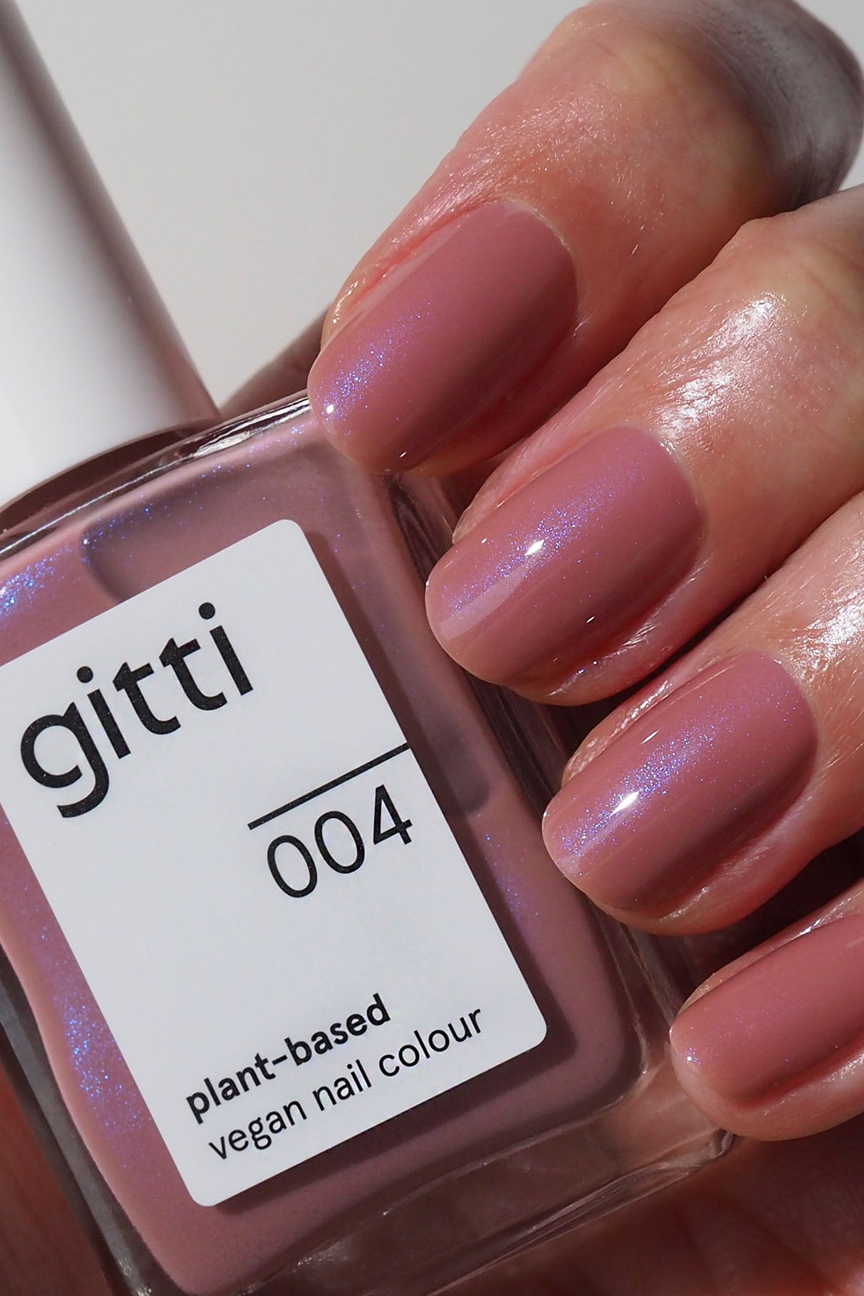 Eine Hand mit kurzen, sauber manikürten, lila-rosa lackierten Nägeln hält eine Flasche mit der Aufschrift Express All-in-One Set, das mit einem High Gloss Top Coat für zusätzlichen Glanz versehen ist.