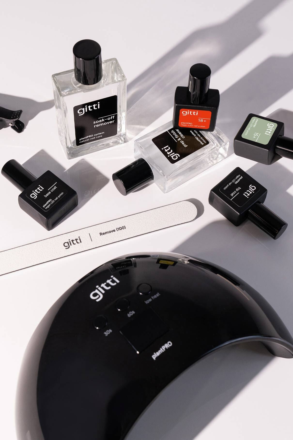 Verschiedene Gitti-Nagelprodukte, darunter Nagellackflaschen, eine Nagelfeile und das plantPRO System + Lampe, sind auf einer weißen Fläche angeordnet.