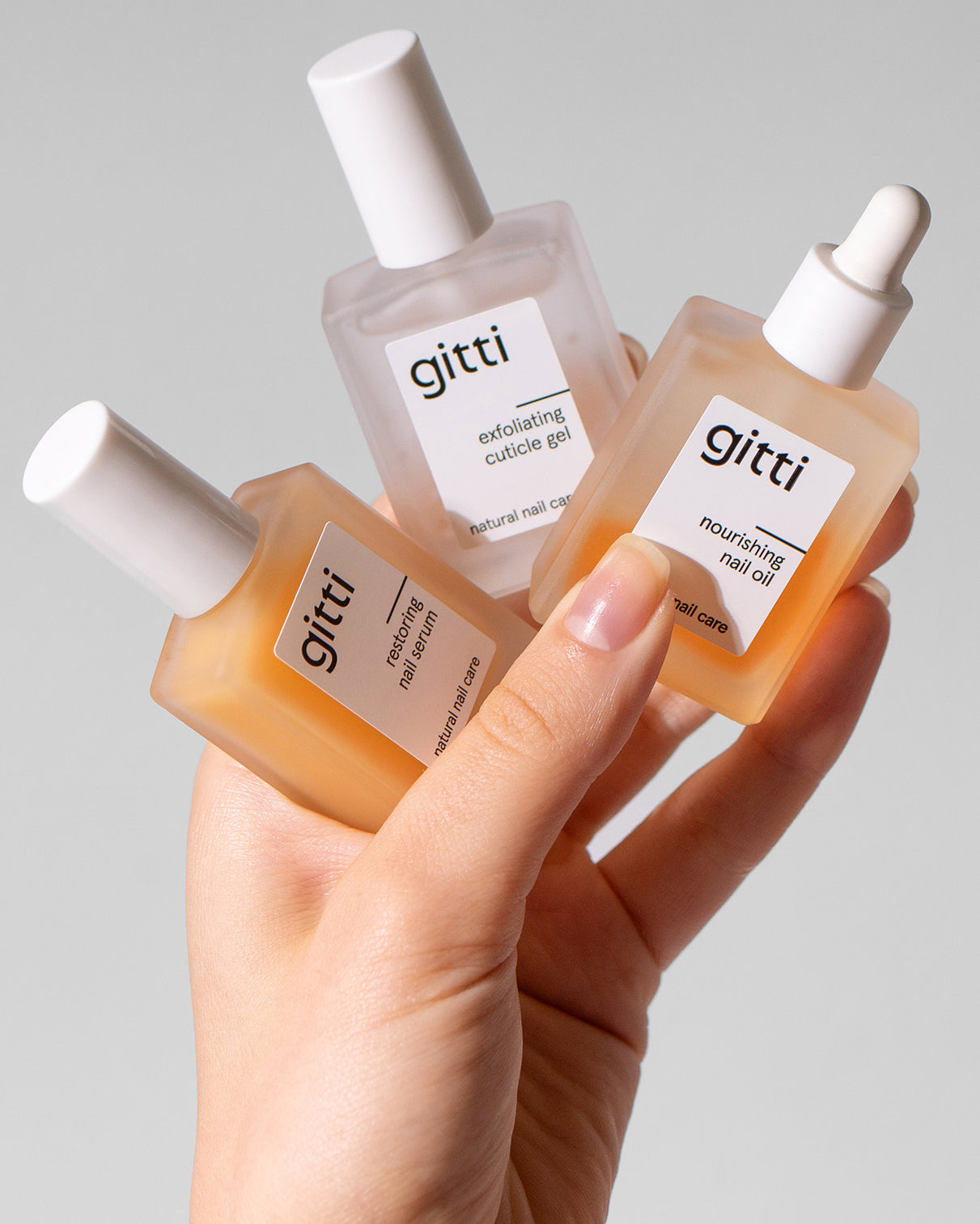 Eine Hand hält die Community Box - drei Gitti Nagelpflegeprodukte in Glasflaschen: Peeling-Häutchen-Gel, Nagel-Essenz und pflegendes Nagelöl mit weißem Verschluss. Jetzt Community Box mit kostenlosem Versand sichern!.