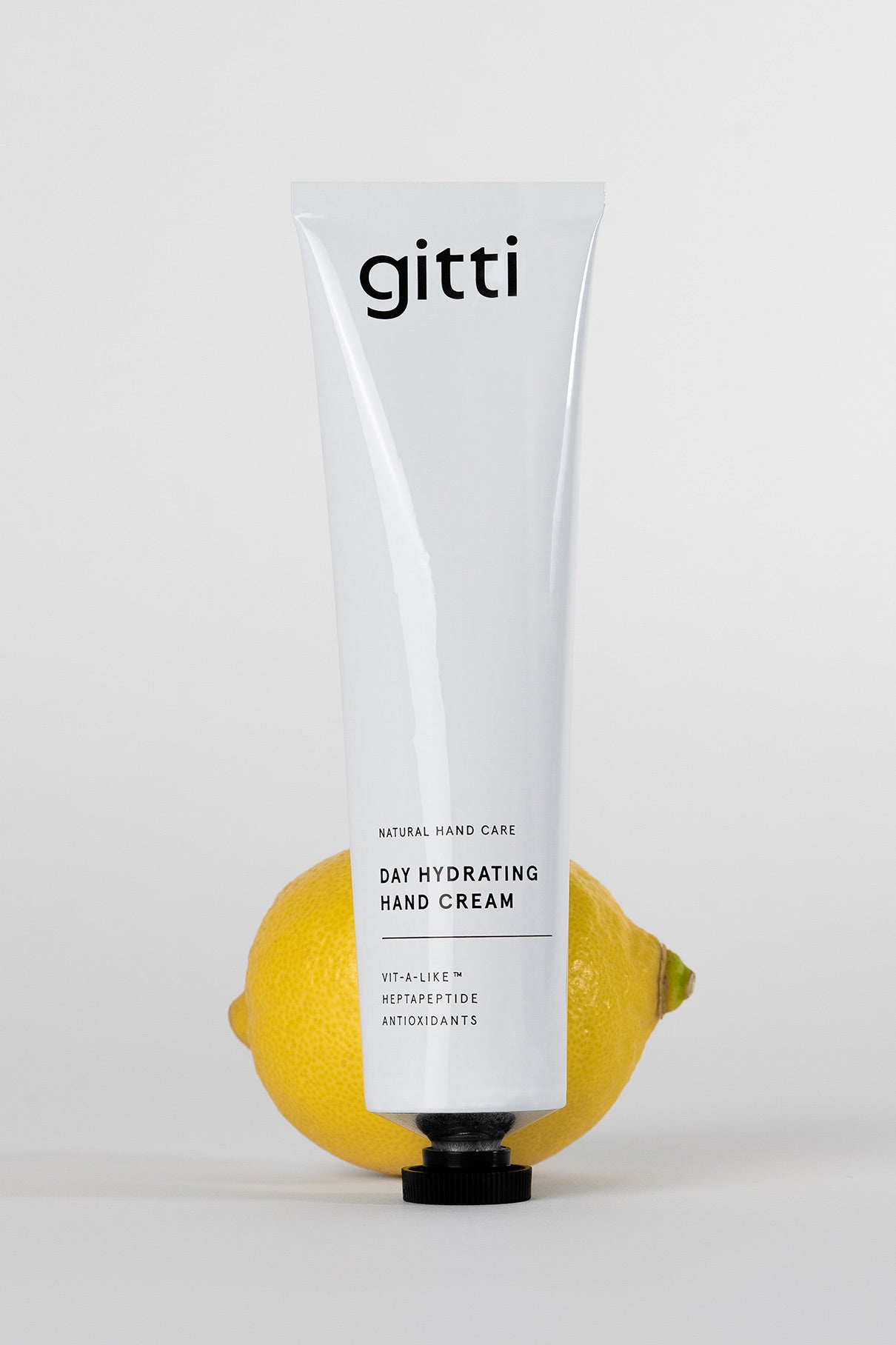 Eine Tube Day Hydrating Hand Cream steht aufrecht mit einer Zitrone dahinter vor einem weißen Hintergrund - die perfekte tägliche Pflege für gepflegte Hände.