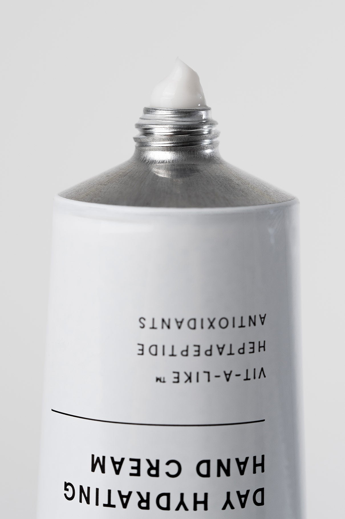 Eine Metalltube der Day Hydrating Hand Cream mit abgenommener Kappe; an der Öffnung ist eine kleine Menge weißer Creme zu sehen, die bereit ist, Ihre Hände mit Feuchtigkeit zu versorgen.