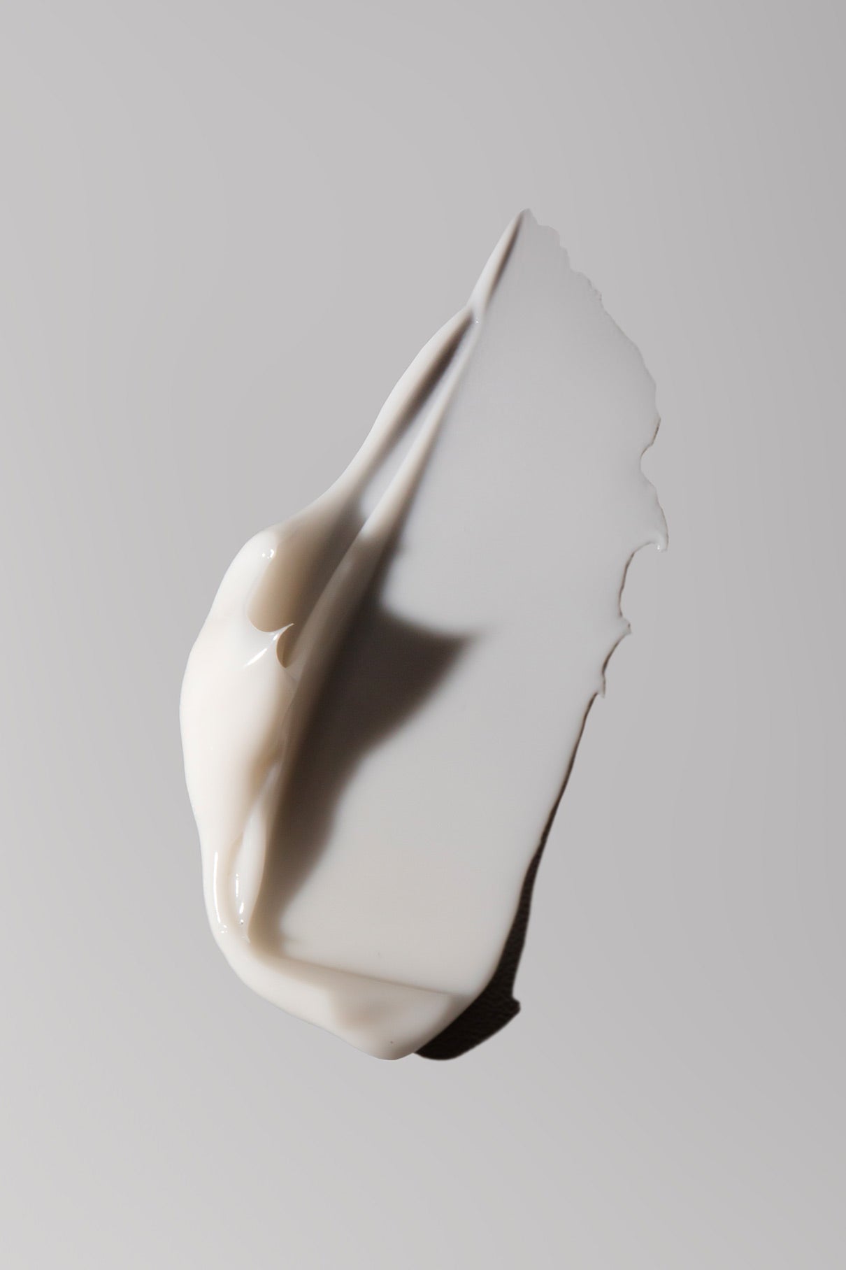 Ein Klecks Day Hydrating Hand Cream auf einer glatten, hellgrauen Oberfläche mit einem sanften Schatten - ideal für die tägliche Handpflege.