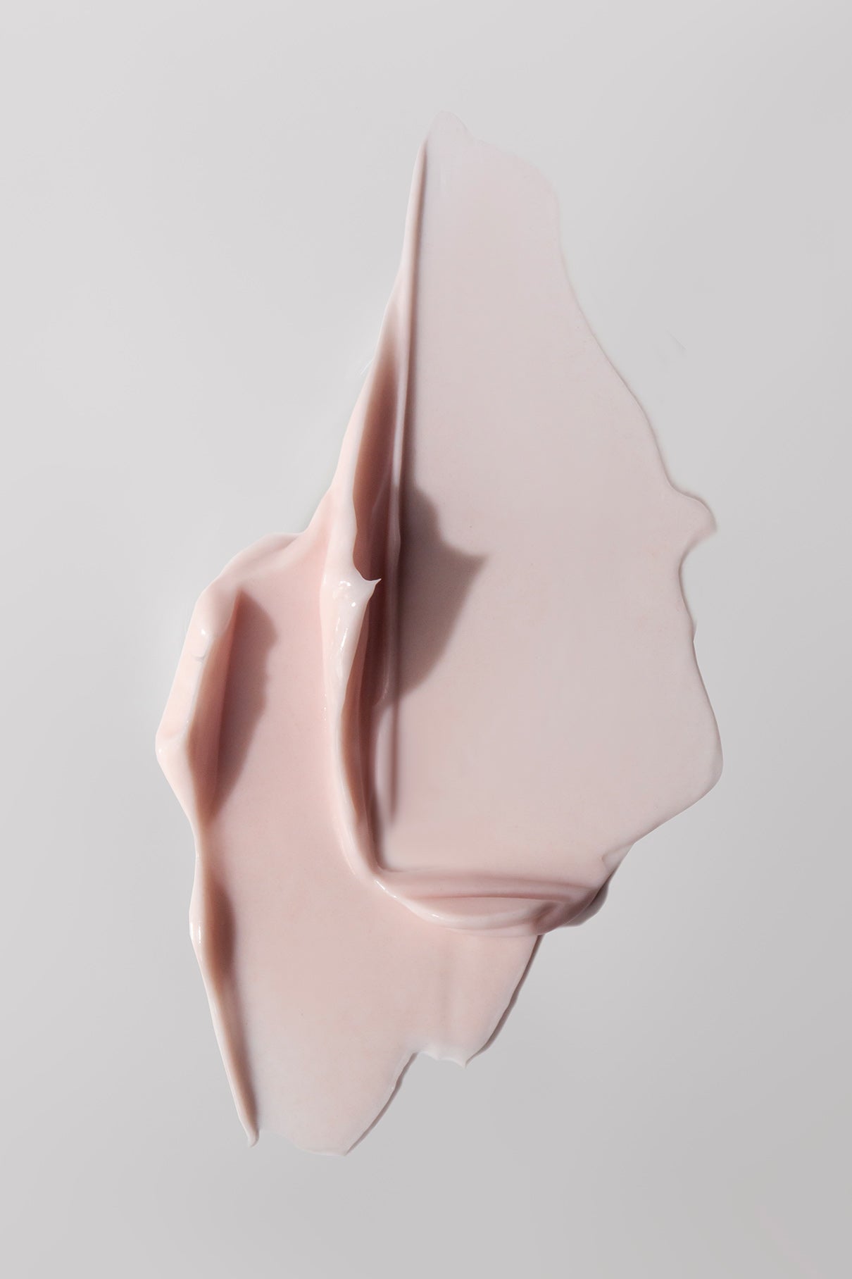 Eine Nahaufnahme eines Abstrichs von blassrosa Silky Hands Duo auf einem neutralen grauen Hintergrund.