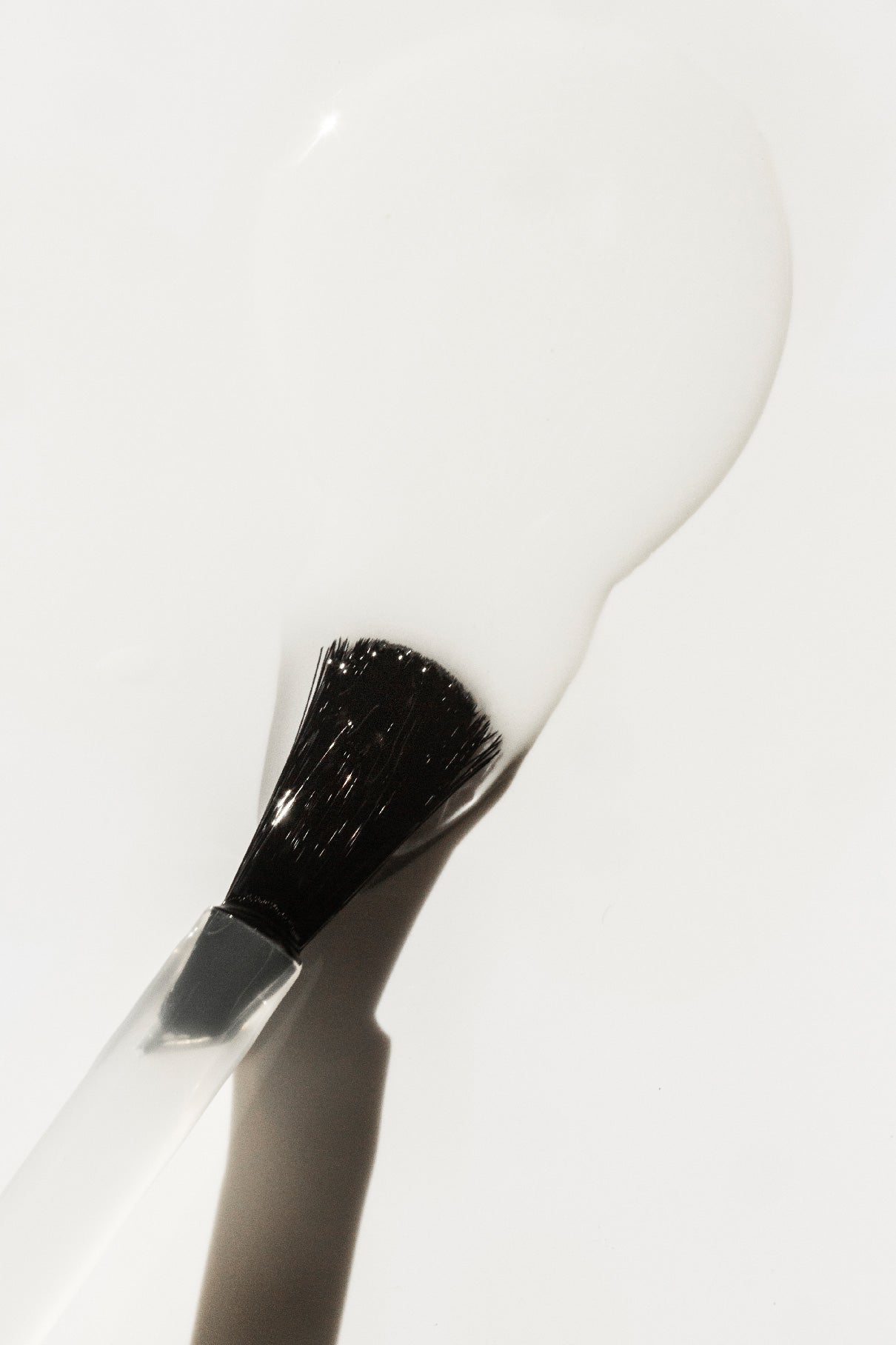 Nahaufnahme eines Pinsels mit schwarzen Borsten und weißem Griff, umhüllt und umgeben von glänzendem weißem Strengthening Nail Hardener, ideal für stärkere Nägel und zur Vorbeugung brüchiger Nägel.