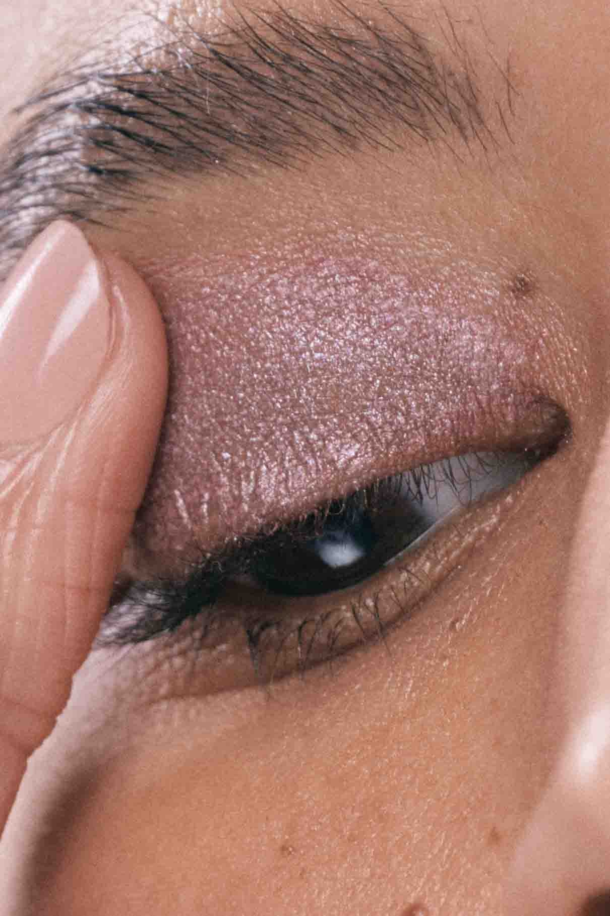 Eine Nahaufnahme des geschlossenen Auges einer Person zeigt den Visionist Nr. 01 Lidschatten in schimmernden Beerentönen, während sie ihr Augenlid sanft mit einem Finger berührt.