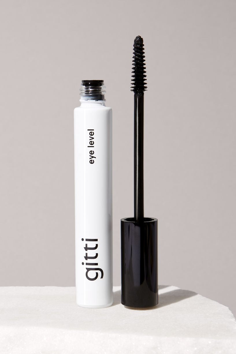 Eine geöffnete Tube Lash Duo Mascara ist abgebildet, wobei der Zauberstab aufrecht neben dem weißen Behälter vor einem neutralen Hintergrund steht.