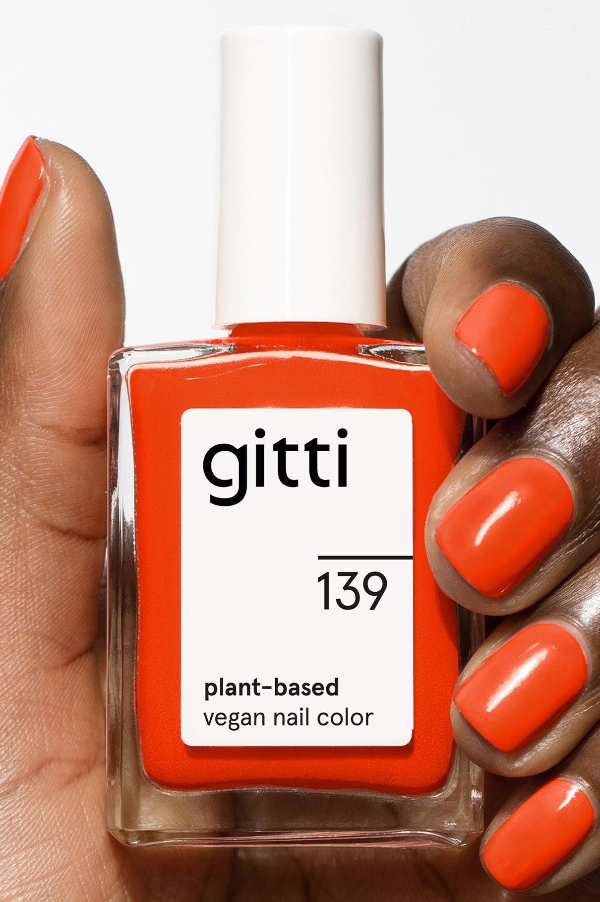 Eine Hand mit orange lackierten Nägeln hält eine Flasche gitti 139 pflanzliche vegane Nagelfarbe in einem passenden Orangeton - entdecke die Community Box mit kostenlosem Versand.