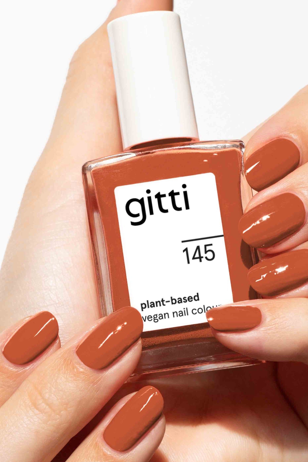 Eine Hand, die eine Flasche gitti no. 145, mit Nägeln, die in demselben warmen Zimtbraun lackiert sind - eine wunderschöne vegane, pflanzliche Nagelfarbe.