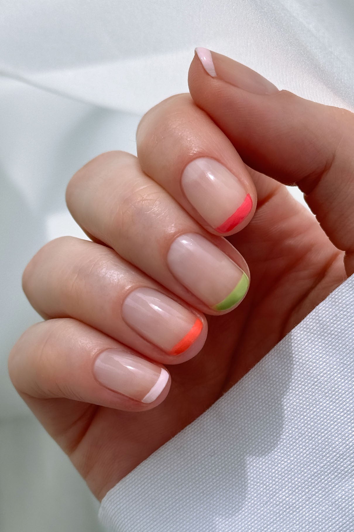 Eine Hand zeigt eine Maniküre mit Naturnägeln und French Tips in Pink, Rot, Orange und Grün - erstellt mit dem Nail Art Set - vor einem hellen Hintergrund.