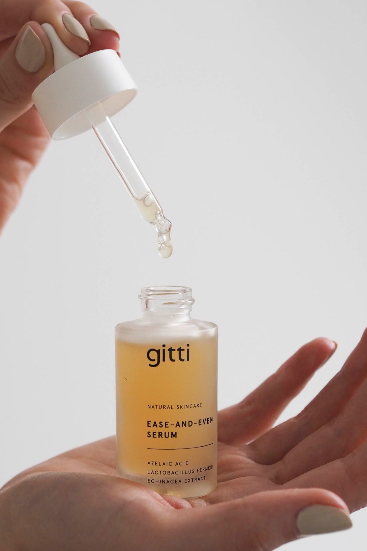 Eine Hand hält eine Pipette über einer geöffneten Flasche mit Ease-and-Even-Serum, in die gleich ein paar Tropfen fallen werden - ideal, um die Ölproduktion auszugleichen und Hautunreinheiten zu reduzieren.