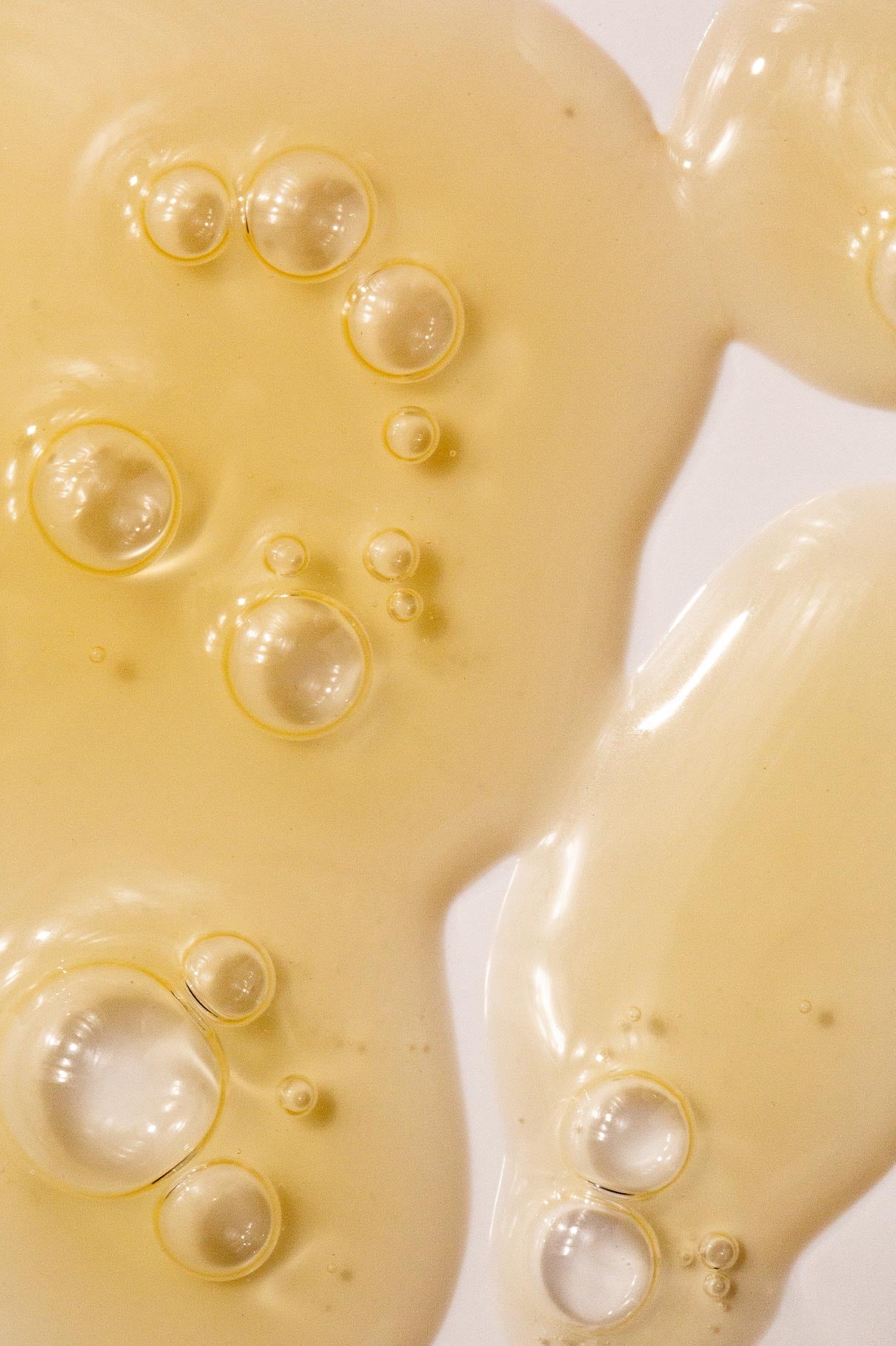 Nahaufnahme einer gelblichen Flüssigkeit mit Blasen auf einem glatten weißen Hintergrund, die die Textur und Klarheit widerspiegelt, die mit dem Ease-and-Even-Serum erreicht wurde - ideal zum Ausgleich der Talgproduktion und zur Behandlung von Hautunreinheiten.