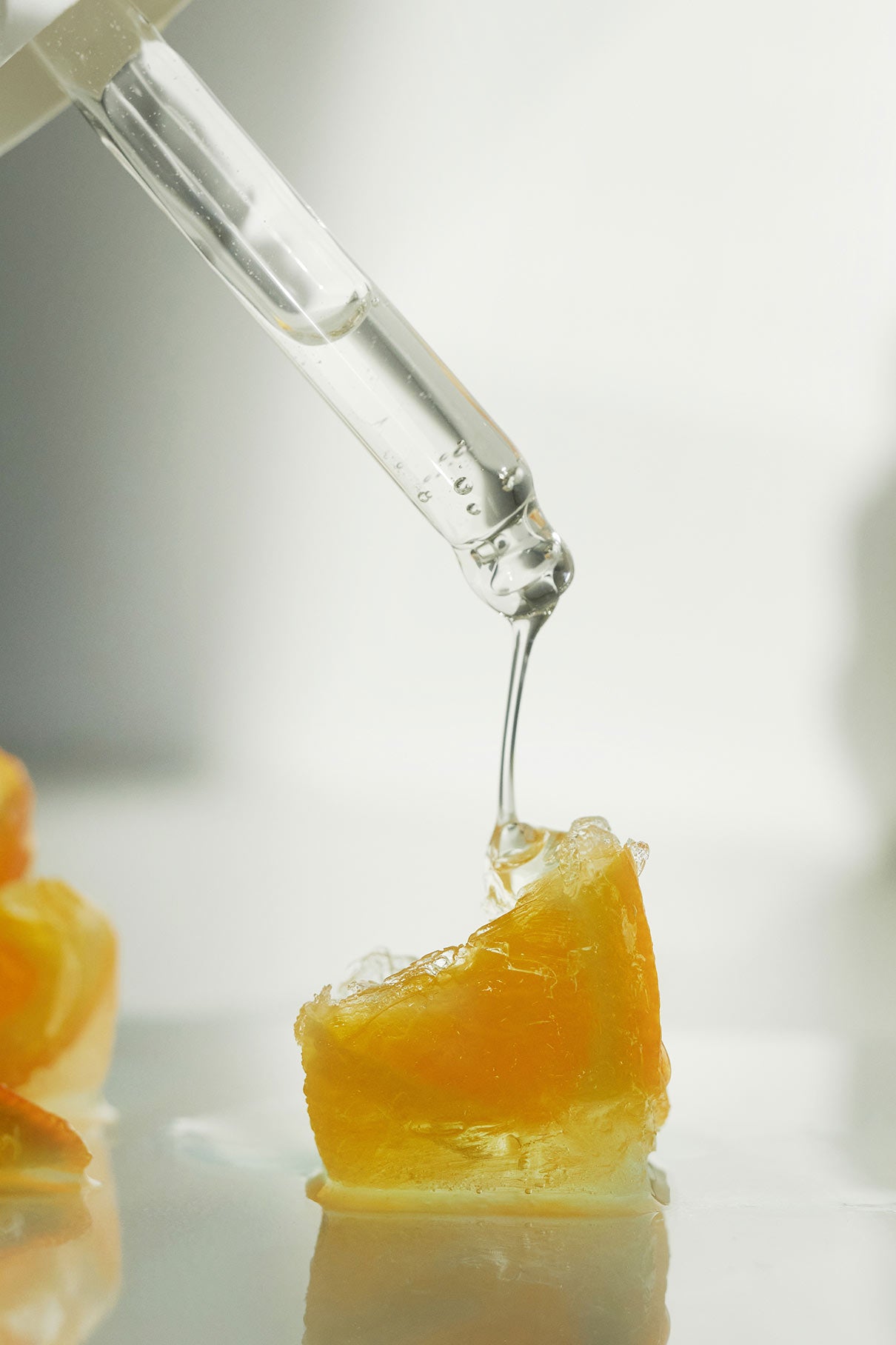 Eine Pipette trägt das Glow-And-Protect Serum auf die Orangenfrucht auf, um die Vorteile der Feuchtigkeit und des Schutzes vor blauem Licht vor einem weichen, hellen Hintergrund zu präsentieren.