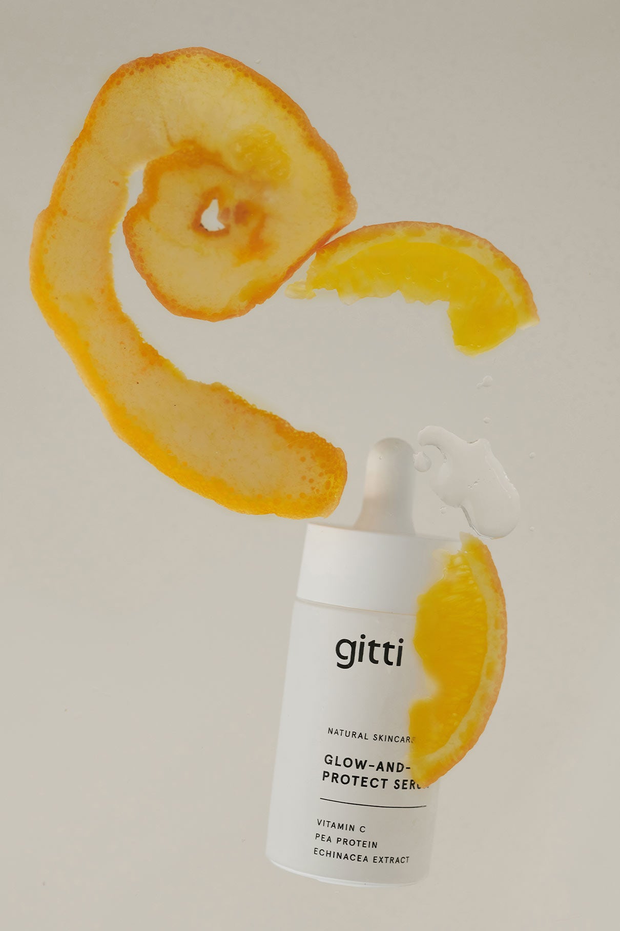 Eine weiße Tropfflasche mit dem Glow-And-Protect Serum steht vor einem neutralen Hintergrund mit Orangenschalen und einer schwebenden Orangenscheibe - Ihr tägliches Serum für Feuchtigkeit und Schutz vor blauem Licht.