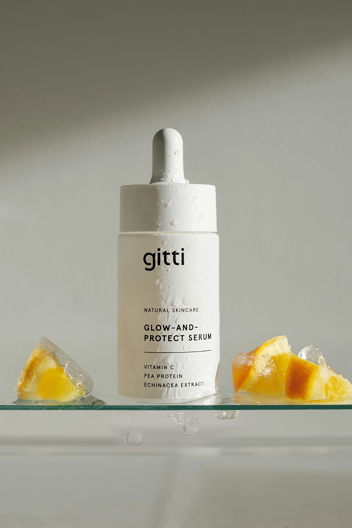 Ein weißer Flakon des Glow-And-Protect-Serums steht aufrecht auf einer Glasfläche mit Eiswürfeln und Fruchtstücken, die seine feuchtigkeitsspendenden Eigenschaften und seinen Schutz vor blauem Licht unterstreichen.