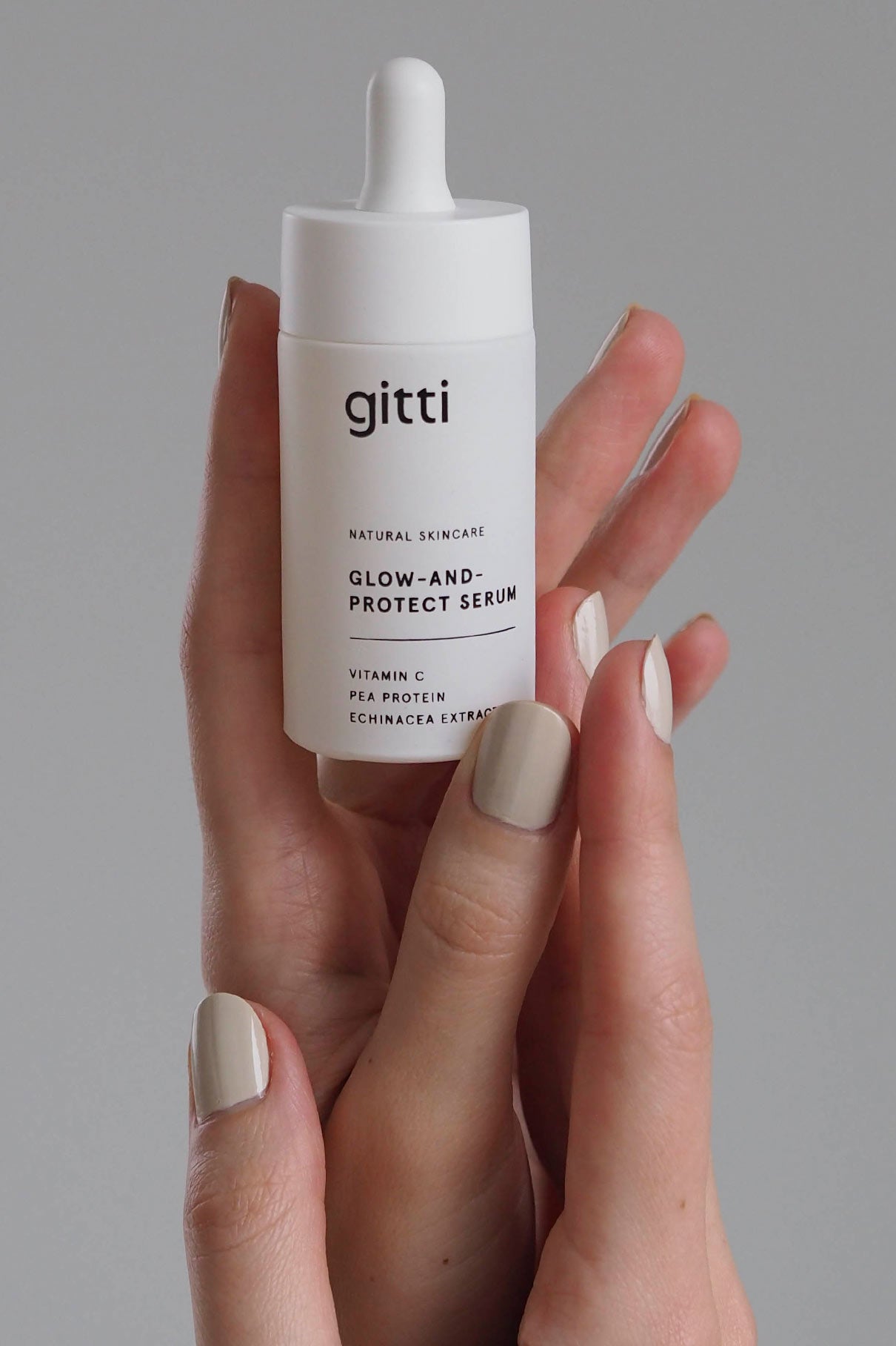 Eine Hand mit hellbeigen Nägeln hält eine Flasche des Glow-And-Protect Serums, das mit Vitamin C, Erbsenprotein und Echinacea-Extrakt Feuchtigkeit spendet und vor blauem Licht schützt.