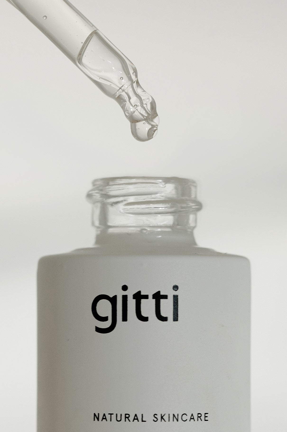 Ein Glastropfer spendet Flüssigkeit über einer offenen weißen Flasche mit der Aufschrift Glow-And-Protect Serum, das Feuchtigkeit spendet und vor blauem Licht schützt, vor einem schlichten Hintergrund.