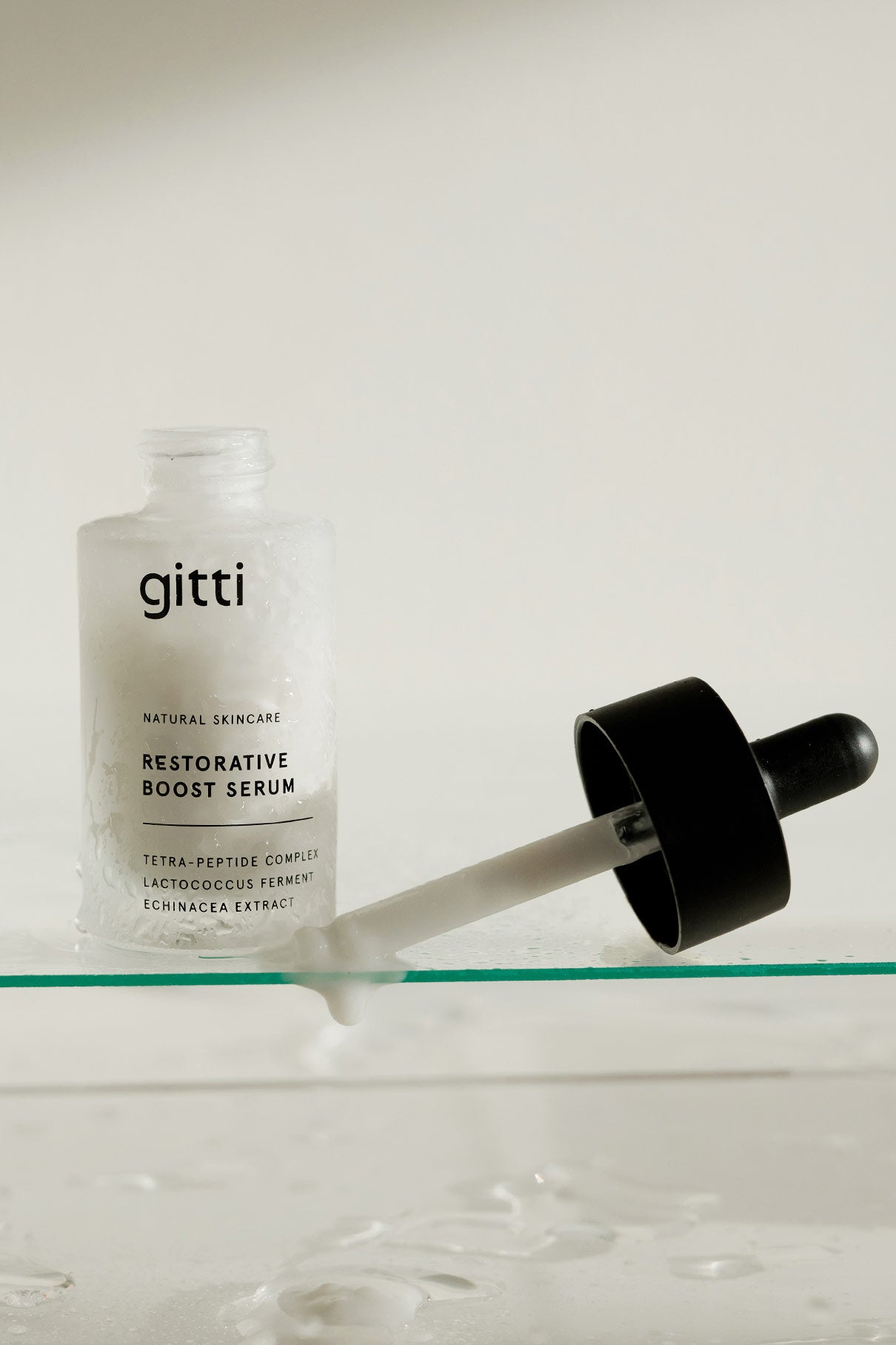 Ein durchsichtiges Fläschchen mit der Aufschrift Restorative Boost Serum" steht neben einem Glastropfer auf einer feuchten Oberfläche und unterstreicht sein Versprechen, die Feuchtigkeitszufuhr und die Elastizität der Haut zu verbessern.