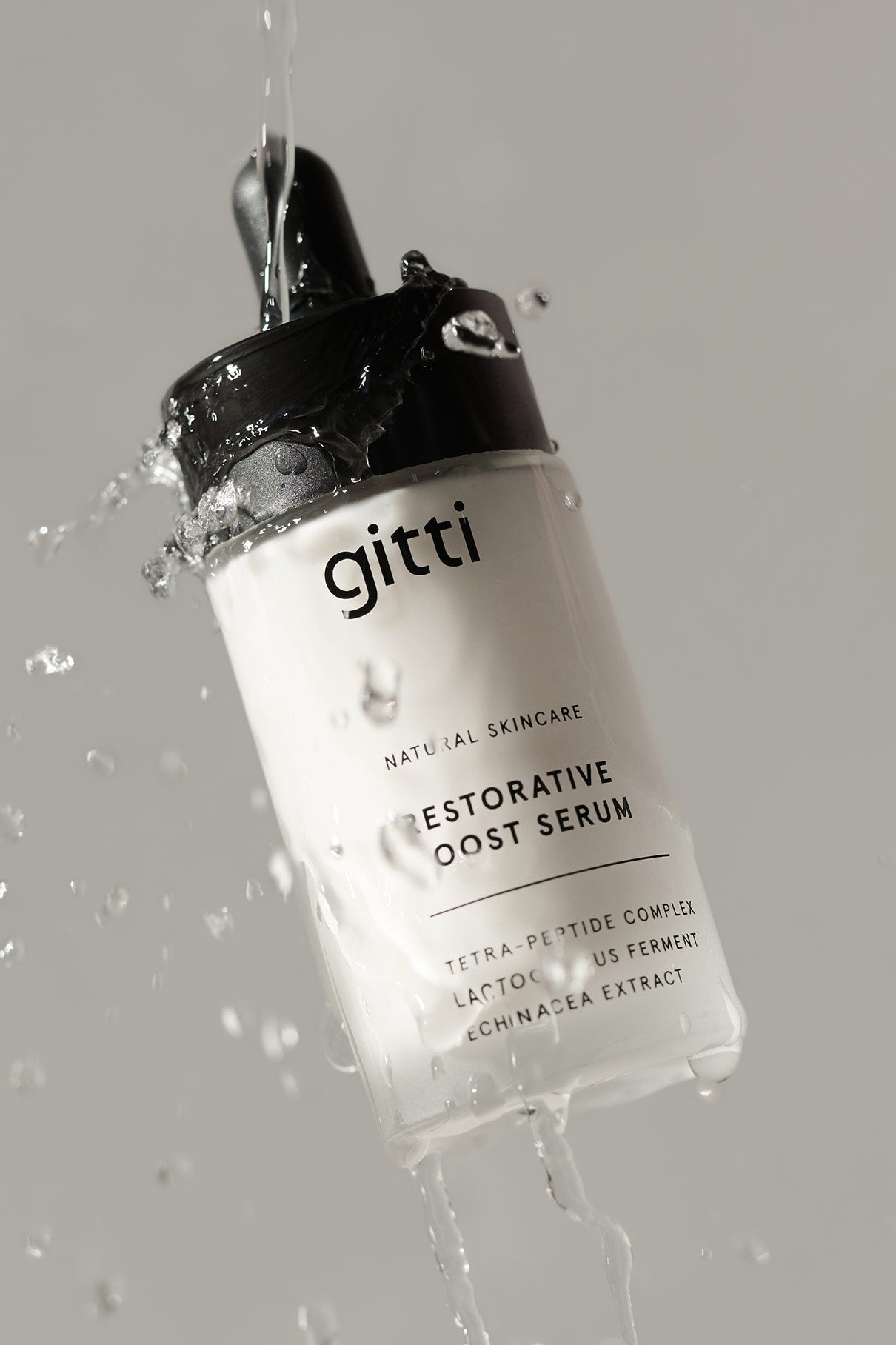 Eine Flasche Restorative Boost Serum mit Wasserspritzern, die Feuchtigkeit und Elastizität der Haut betonen, fotografiert vor einem hellgrauen Hintergrund.