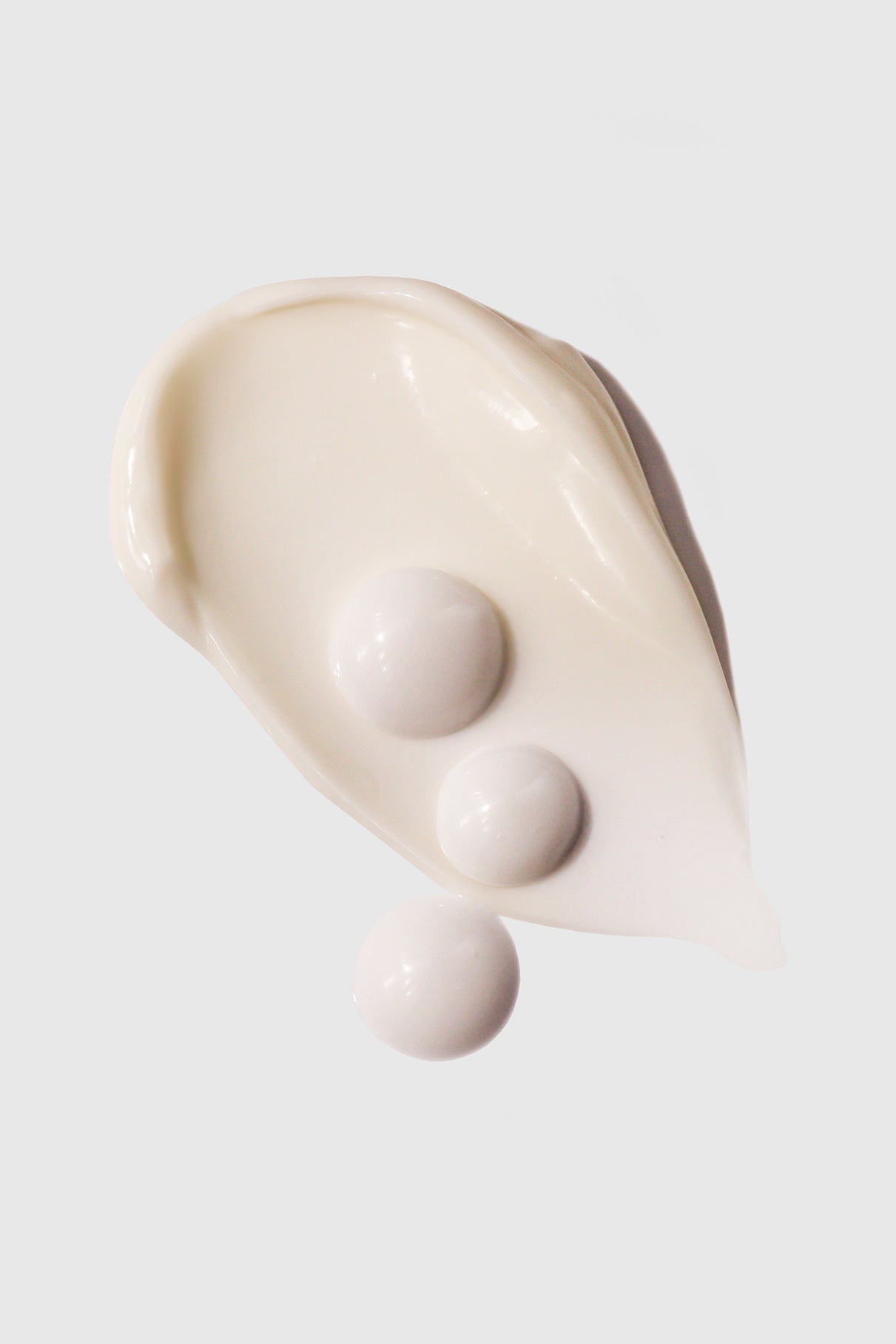 Ein Abstrich von Restore + Hydrate Duo Feuchtigkeitscreme mit drei runden weißen Pillen darauf, vor einem schlichten hellgrauen Hintergrund.