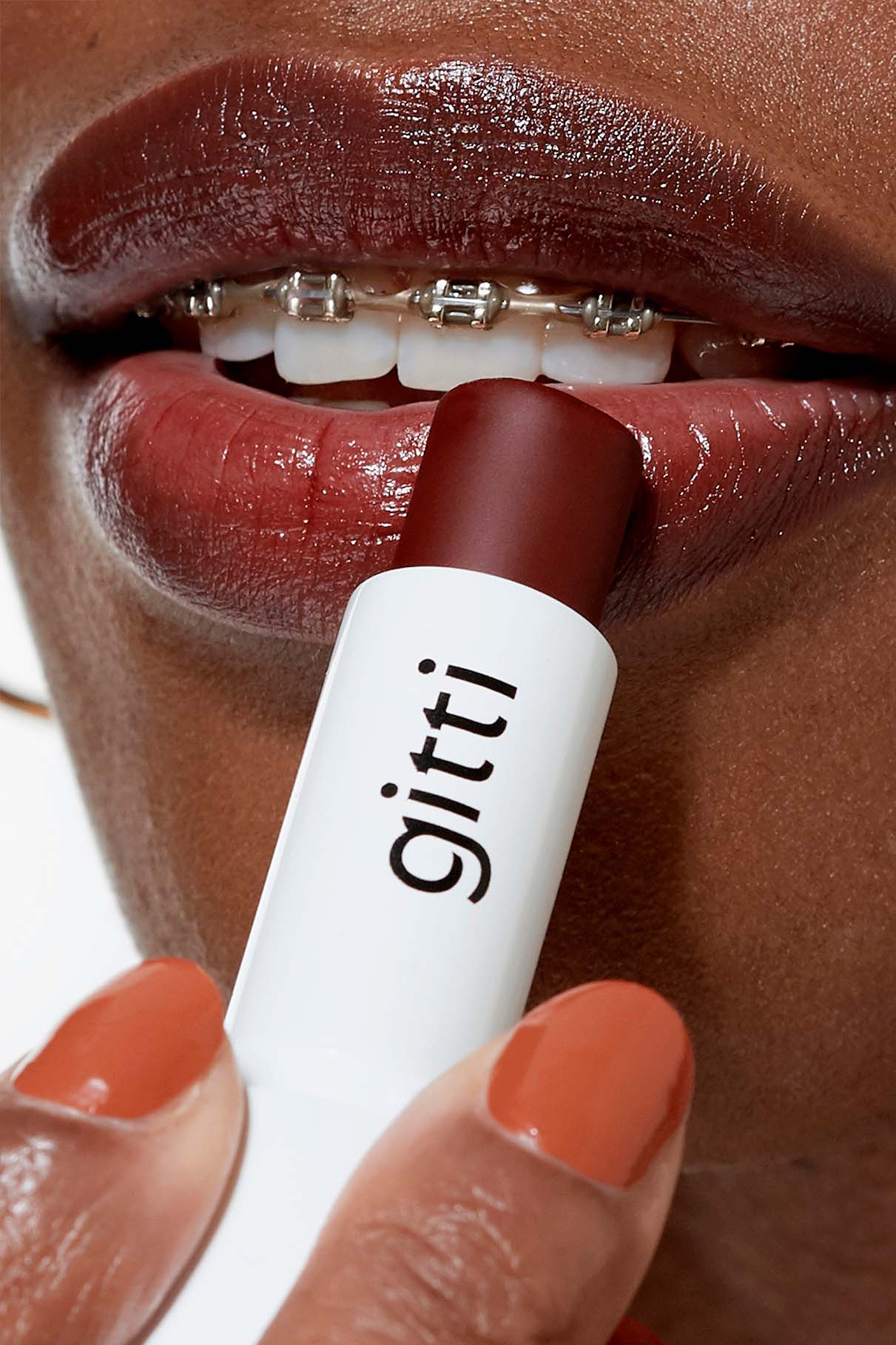 Nahaufnahme einer Person mit Zahnspange, die dunkelroten Nails + Lips in Sync-Lippenstift aufträgt, orangefarbener Lack auf den Fingernägeln - ein perfektes Duo für Ihr nächstes Lip Sync-Set.