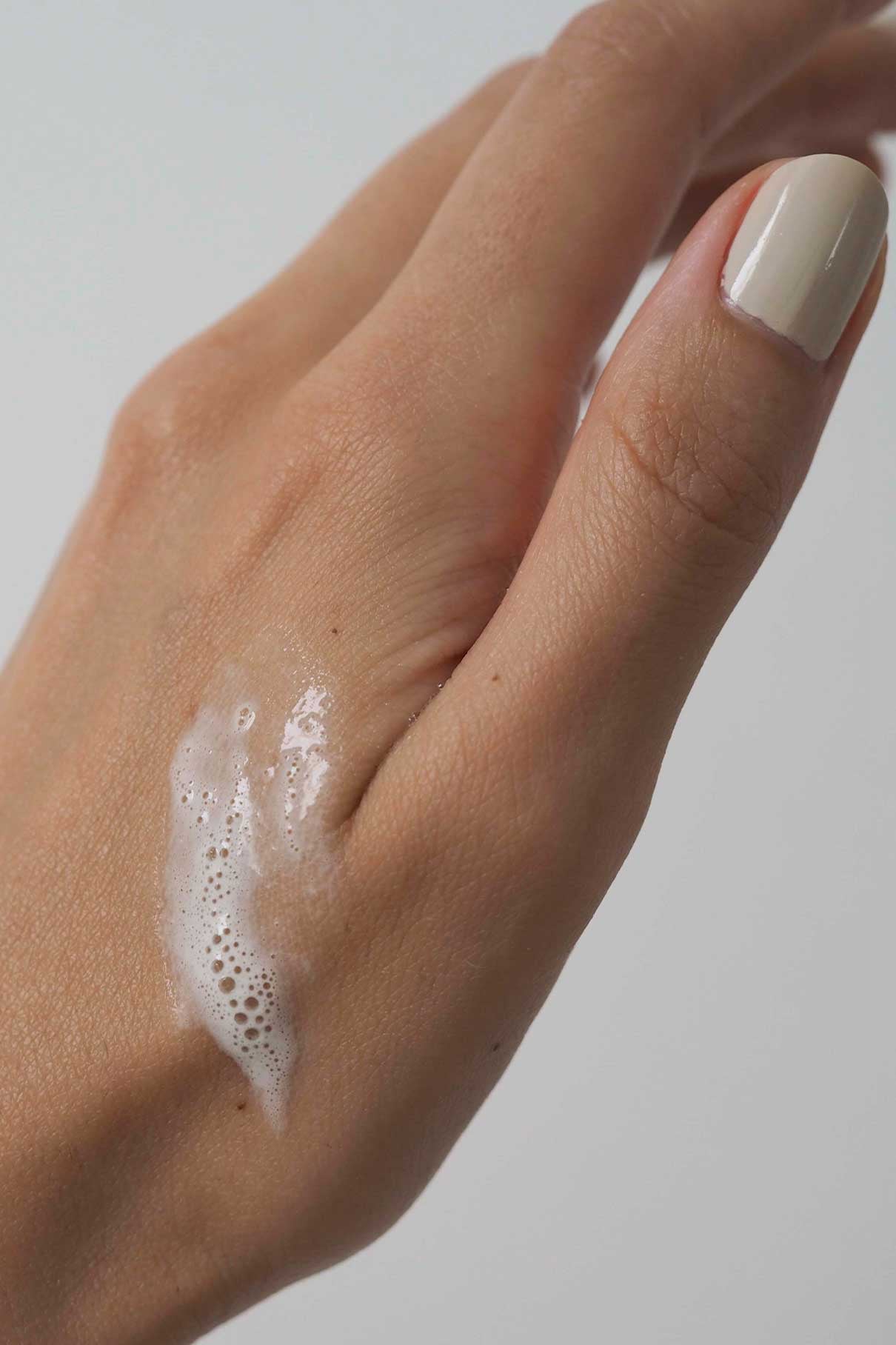 Eine Nahaufnahme einer Hand mit einem hellen Nagel und einer kleinen Menge des schaumigen Skin-Refining Exfoliator, der auf den Handrücken aufgetragen wurde.