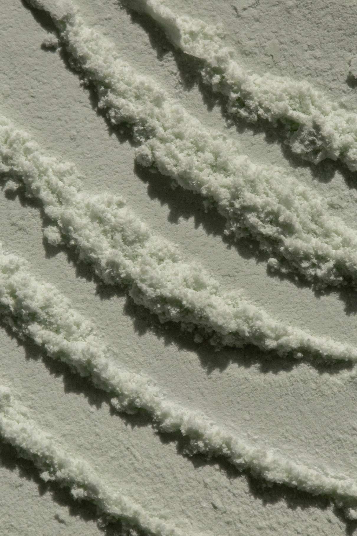 Nahaufnahme mehrerer paralleler Linien in einer feinen, weißen, pudrigen Substanz auf einer flachen Oberfläche, die an die Textur des Skin-Refining Exfoliator für die sanfte Reinigung erinnert.