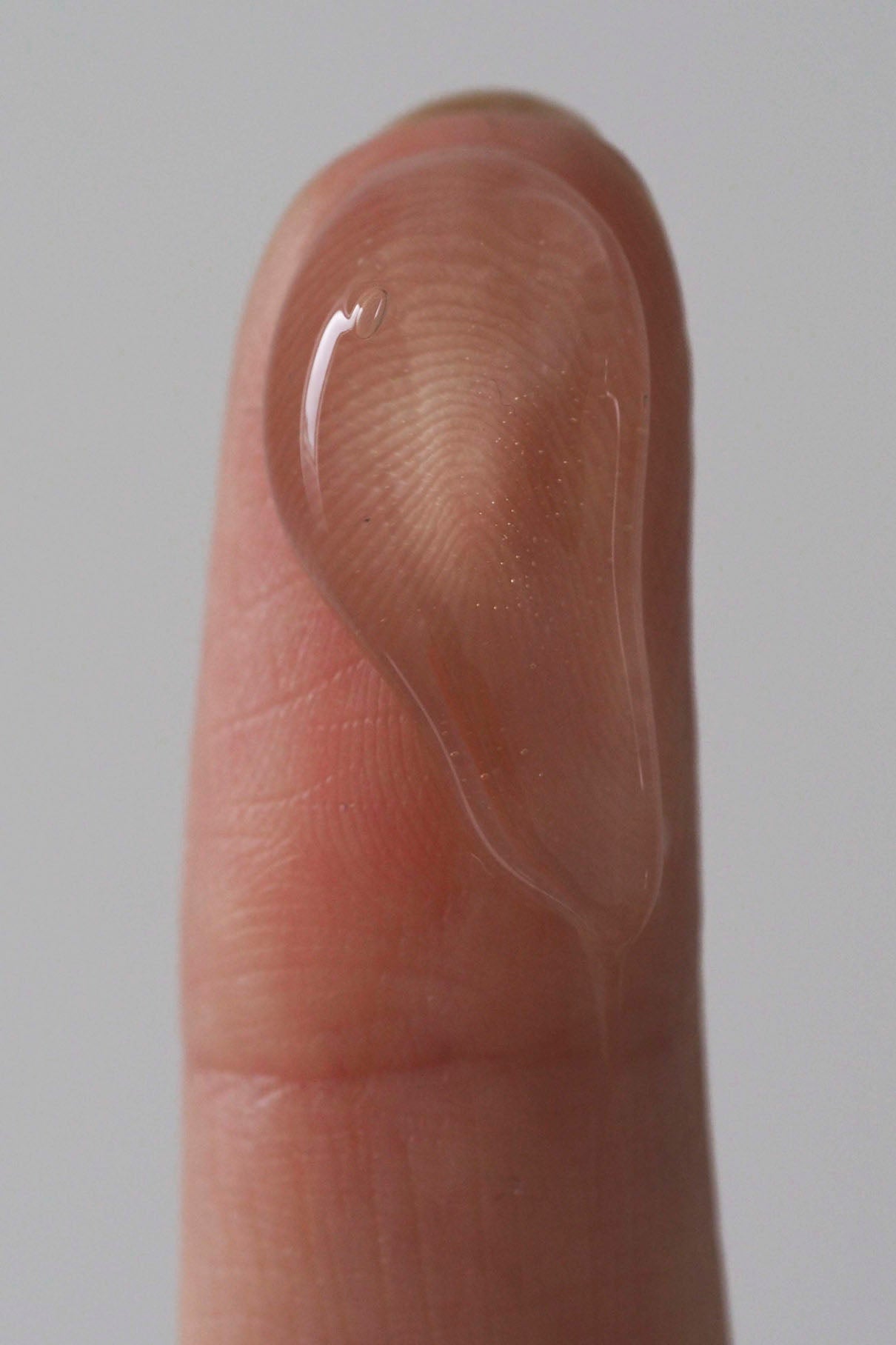 Eine Nahaufnahme einer Fingerspitze mit einem Tropfen klaren Gels vor einem neutralen Hintergrund - perfekt für Ihre Essential Routine.