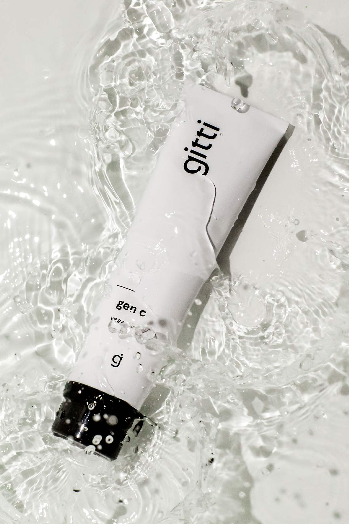 Eine weiße Tube mit der Aufschrift Gen C und einer schwarzen Kappe liegt in spritzendem Wasser. Die Tropfen auf der Oberfläche unterstreichen die effektive und sanfte Reinigungswirkung des Produkts.