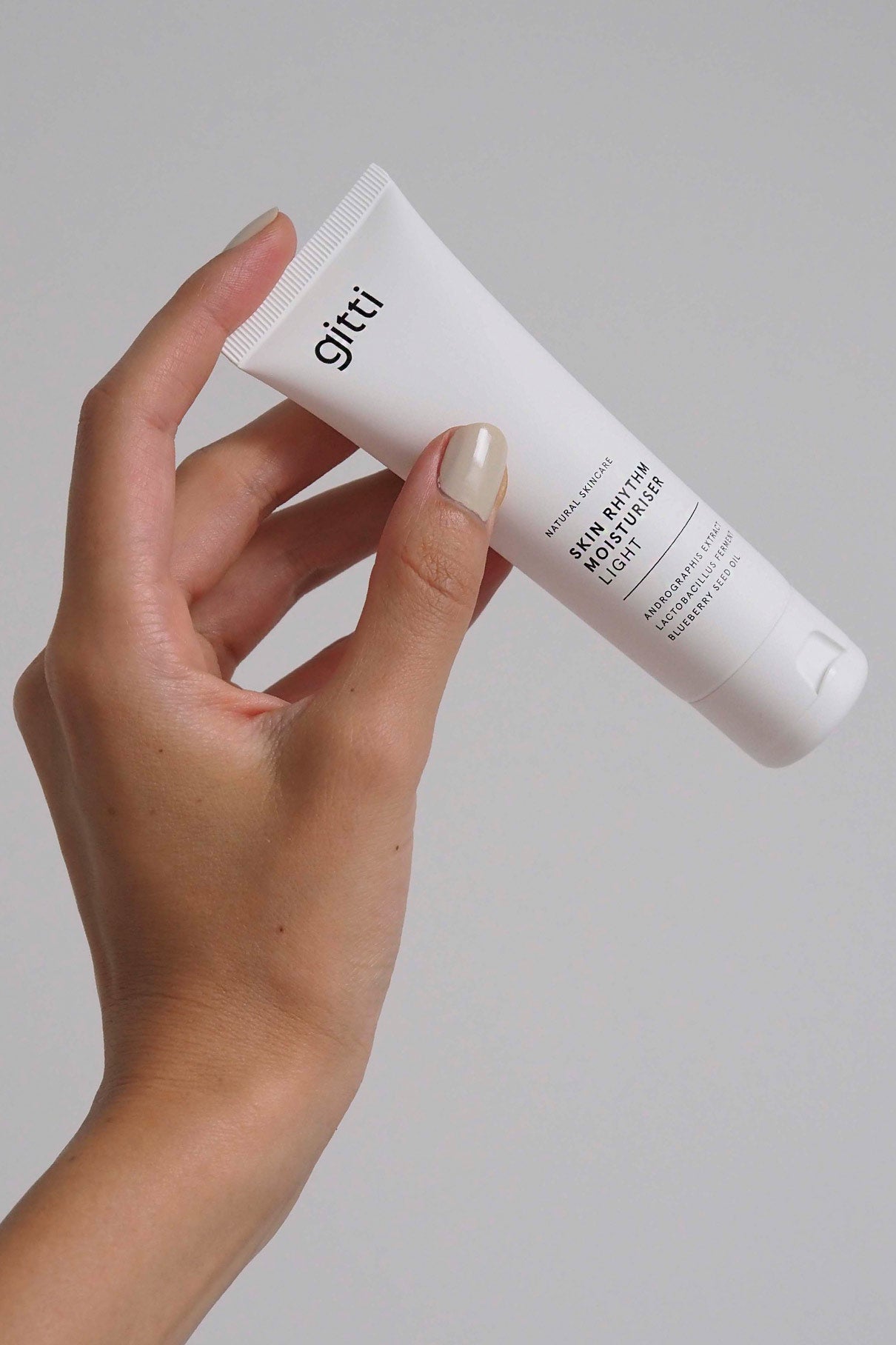 Eine Hand hält eine weiße Tube mit der Aufschrift "Essential Routine" - ein tägliches Beauty-Must-Have - vor einem einfachen, hellen Hintergrund.