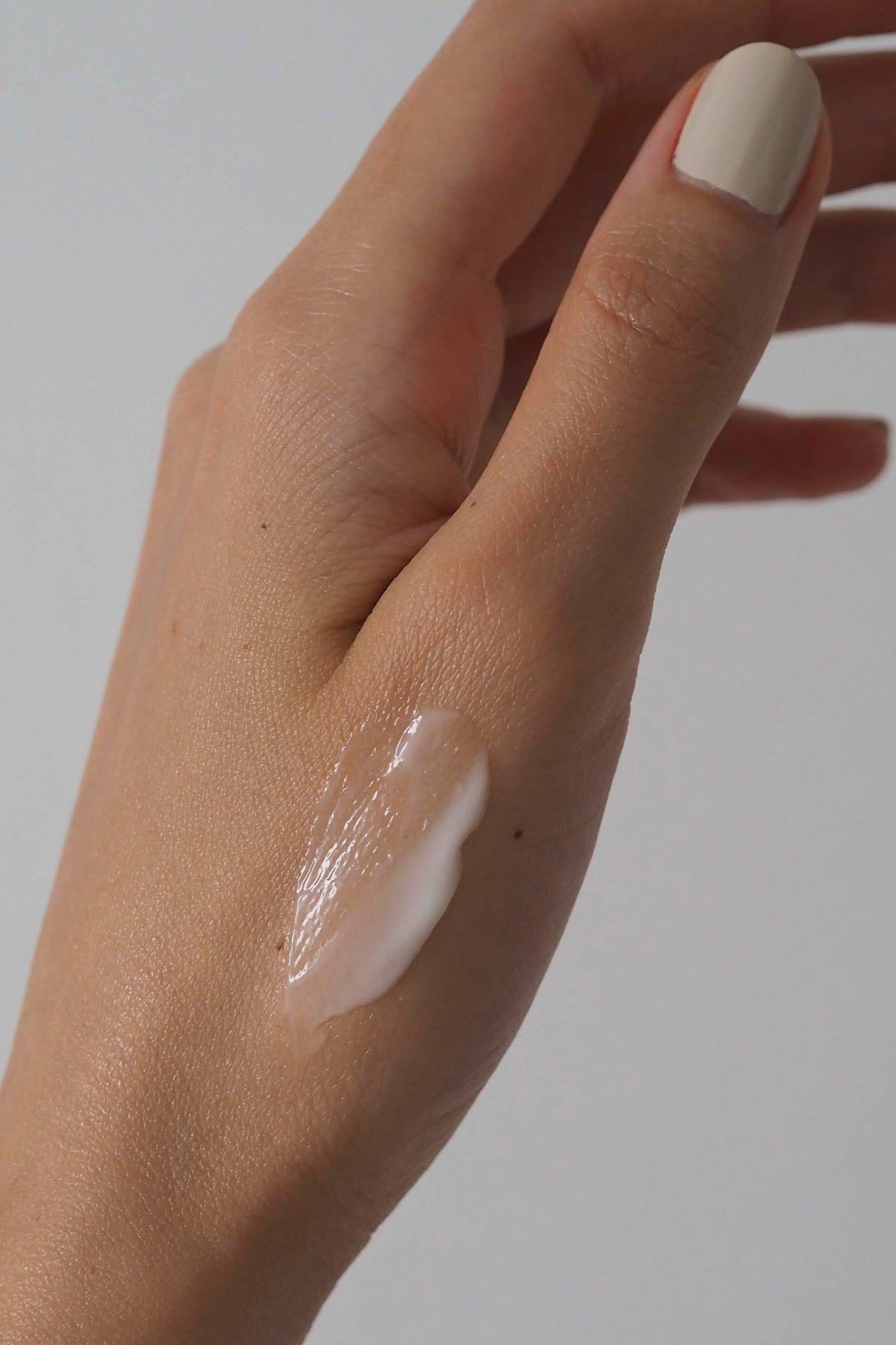 Eine Nahaufnahme einer hellhäutigen Hand mit beigen Nägeln zeigt einen Abstrich der Essential Routine Creme auf dem Handrücken und hebt diesen Pflegeschritt vor einem schlichten Hintergrund hervor.