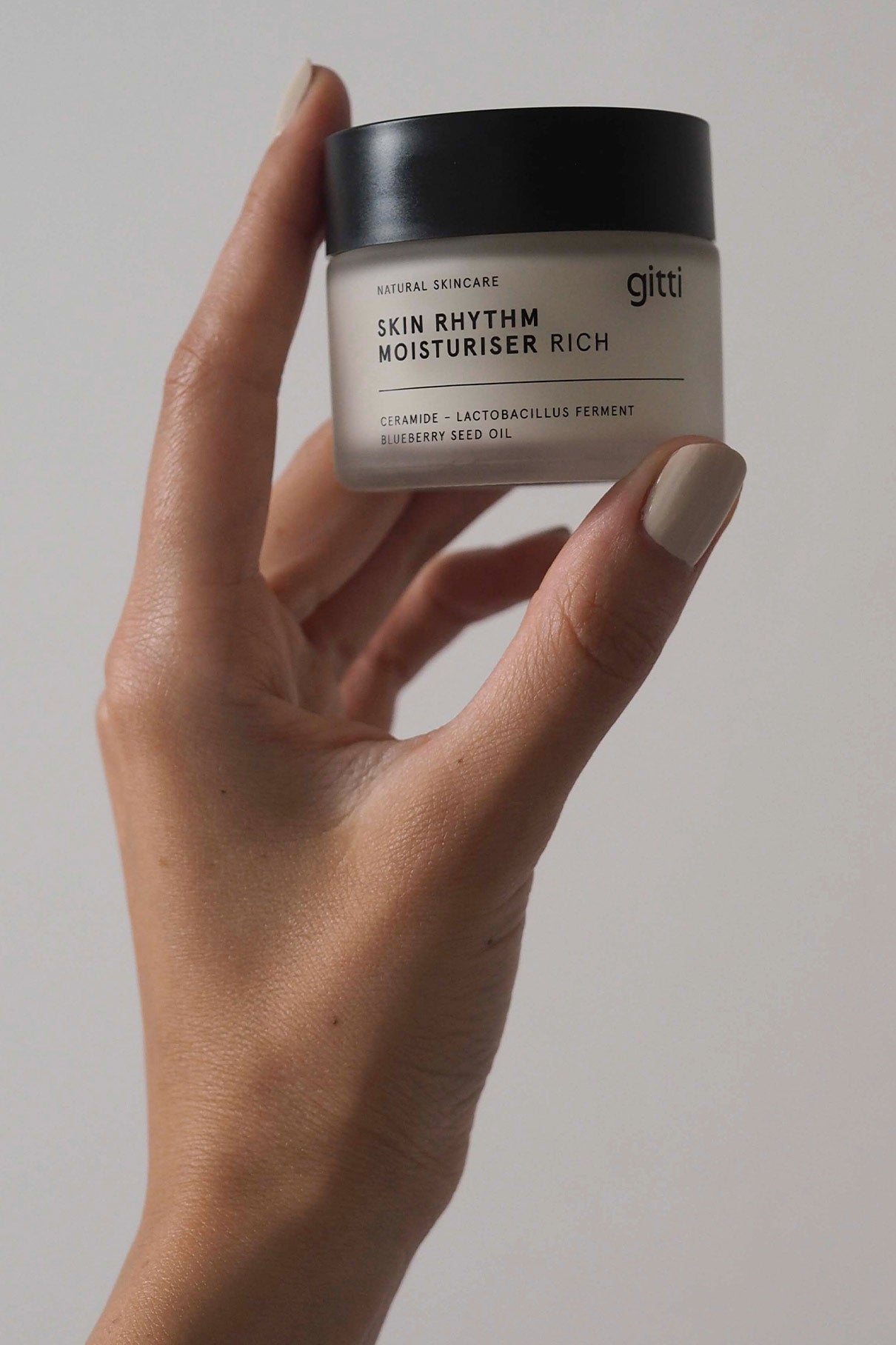 Eine Hand hält einen Tiegel Skin Rhythm Moisturiser Rich vor einem unifarbenen Hintergrund, der den Barriereschutz und die intensive Feuchtigkeitszufuhr für ein natürliches Strahlen präsentiert.