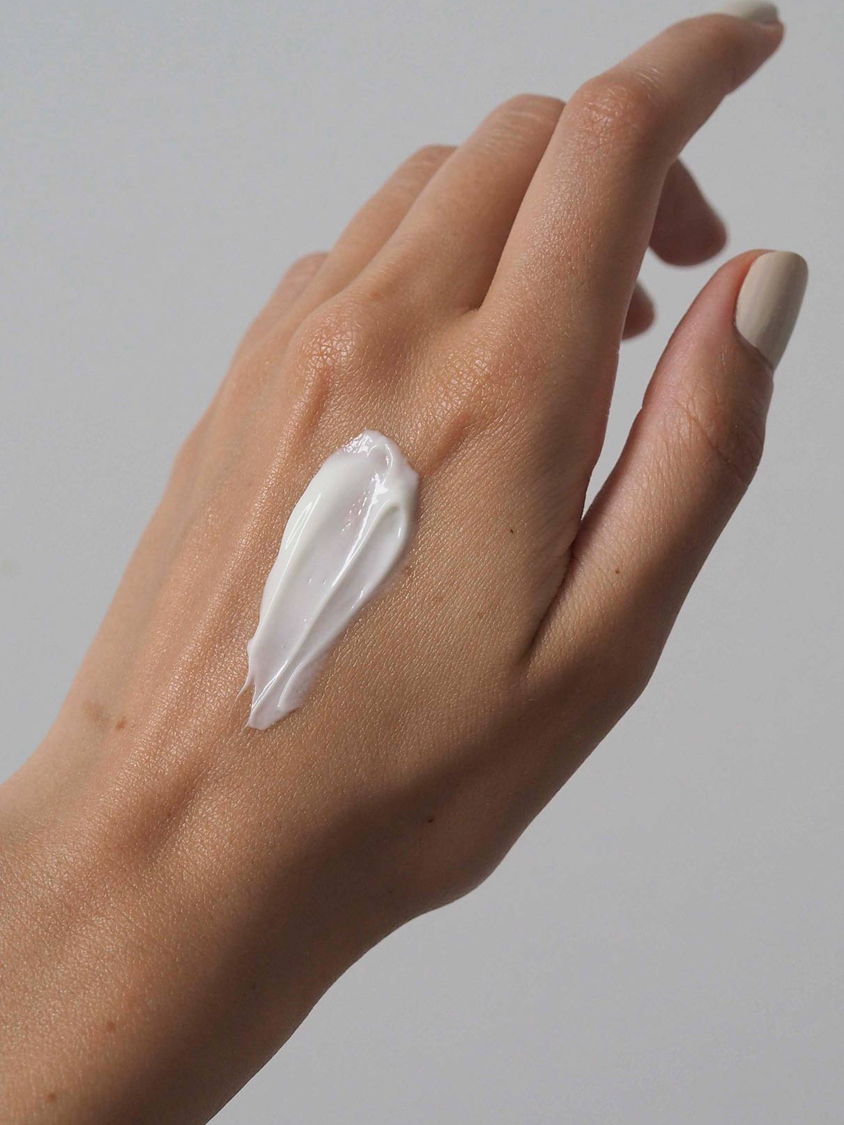 Eine Hand mit hellem Hautton zeigt einen Streifen Skin Rhythm Moisturiser Rich auf dem Rücken, der die Feuchtigkeitspflege und den Barriereschutz betont, vor einem schlichten hellgrauen Hintergrund.