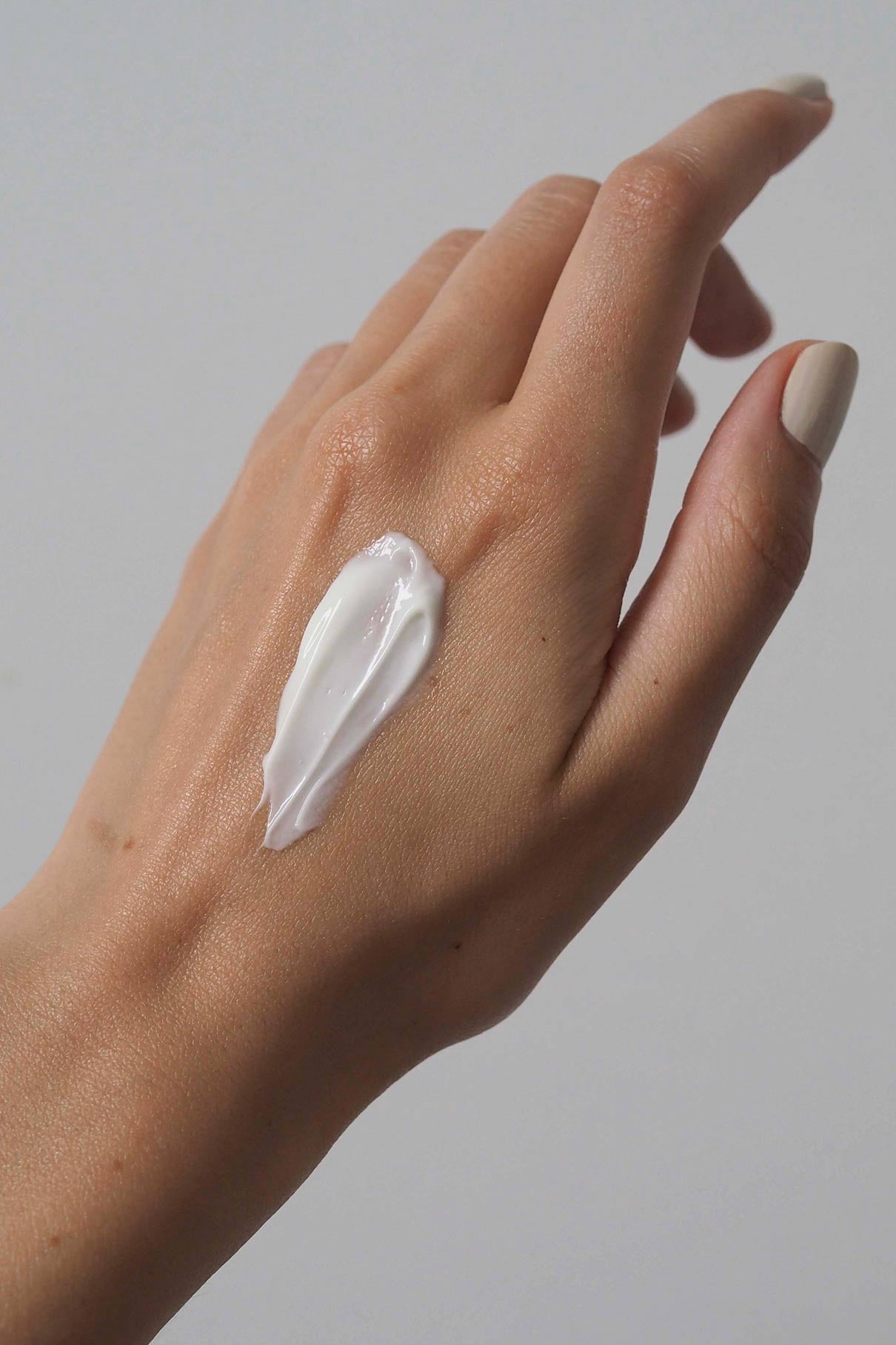 Eine Nahaufnahme einer Hand mit einem weißen Cremestrich auf dem Handrücken, der Essential Routine für Ihre Schönheitspflege vor einem schlichten, hellen Hintergrund hervorhebt.