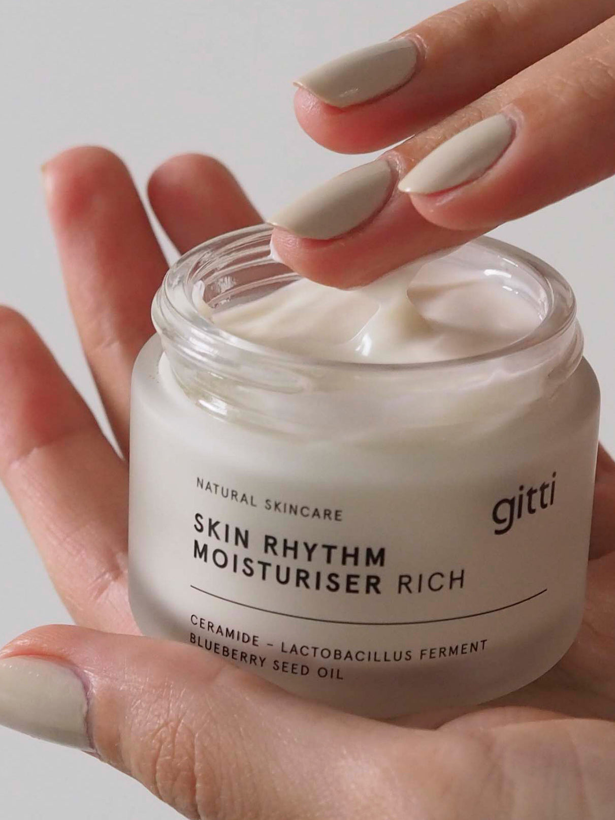 Eine Hand hält einen geöffneten Tiegel Skin Rhythm Moisturiser Rich, während die andere Hand einen Finger in die Creme taucht, die intensive Feuchtigkeit spendet und ein gesundes Strahlen hervorhebt.