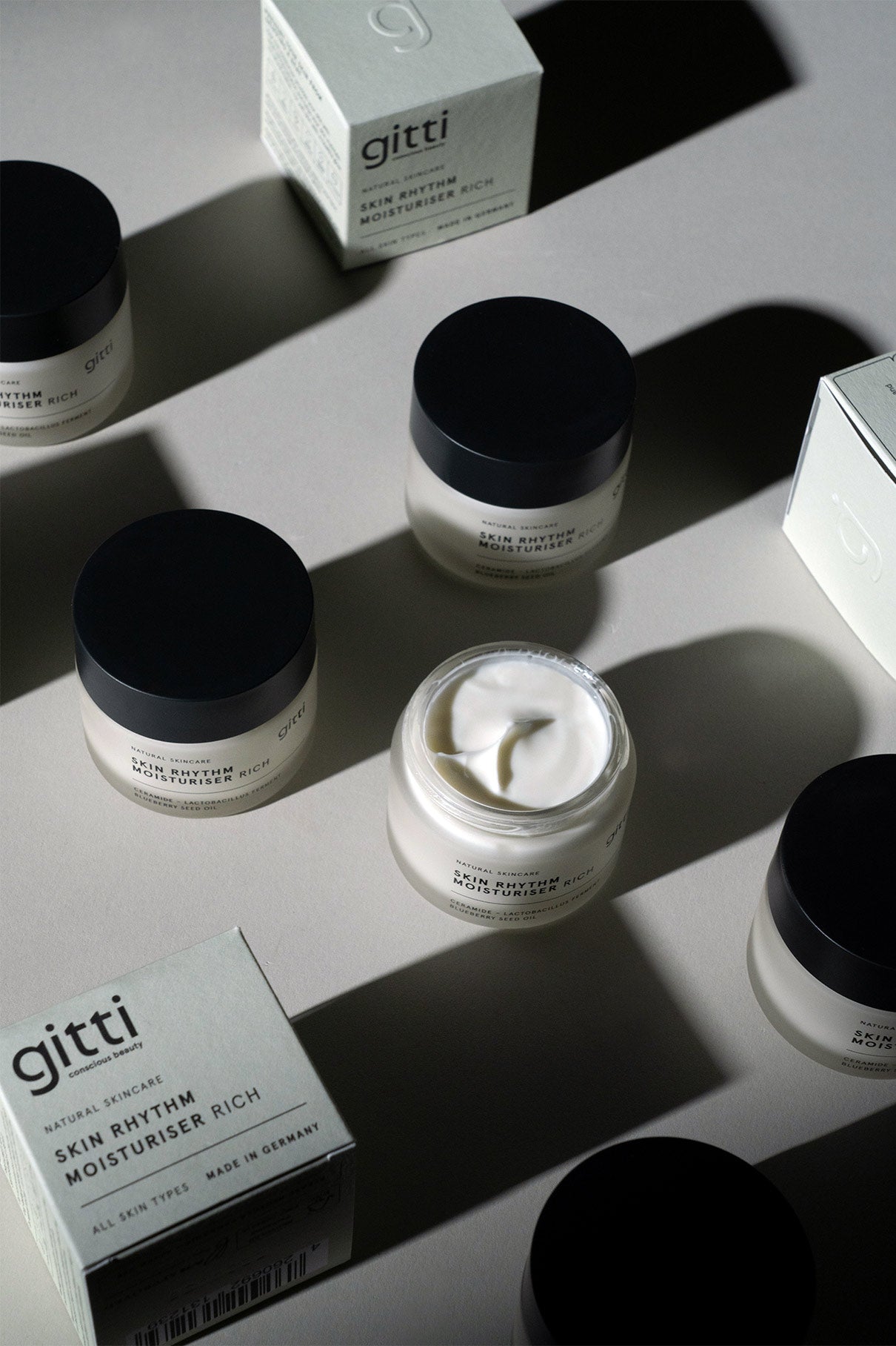 Mehrere Tiegel und Schachteln der Skin Rhythm Moisturiser Rich werden auf einer hellen Fläche ausgestellt, wobei ein geöffneter Tiegel die Creme zeigt - ideal für Feuchtigkeit, Barriereschutz und einen natürlichen Glow.