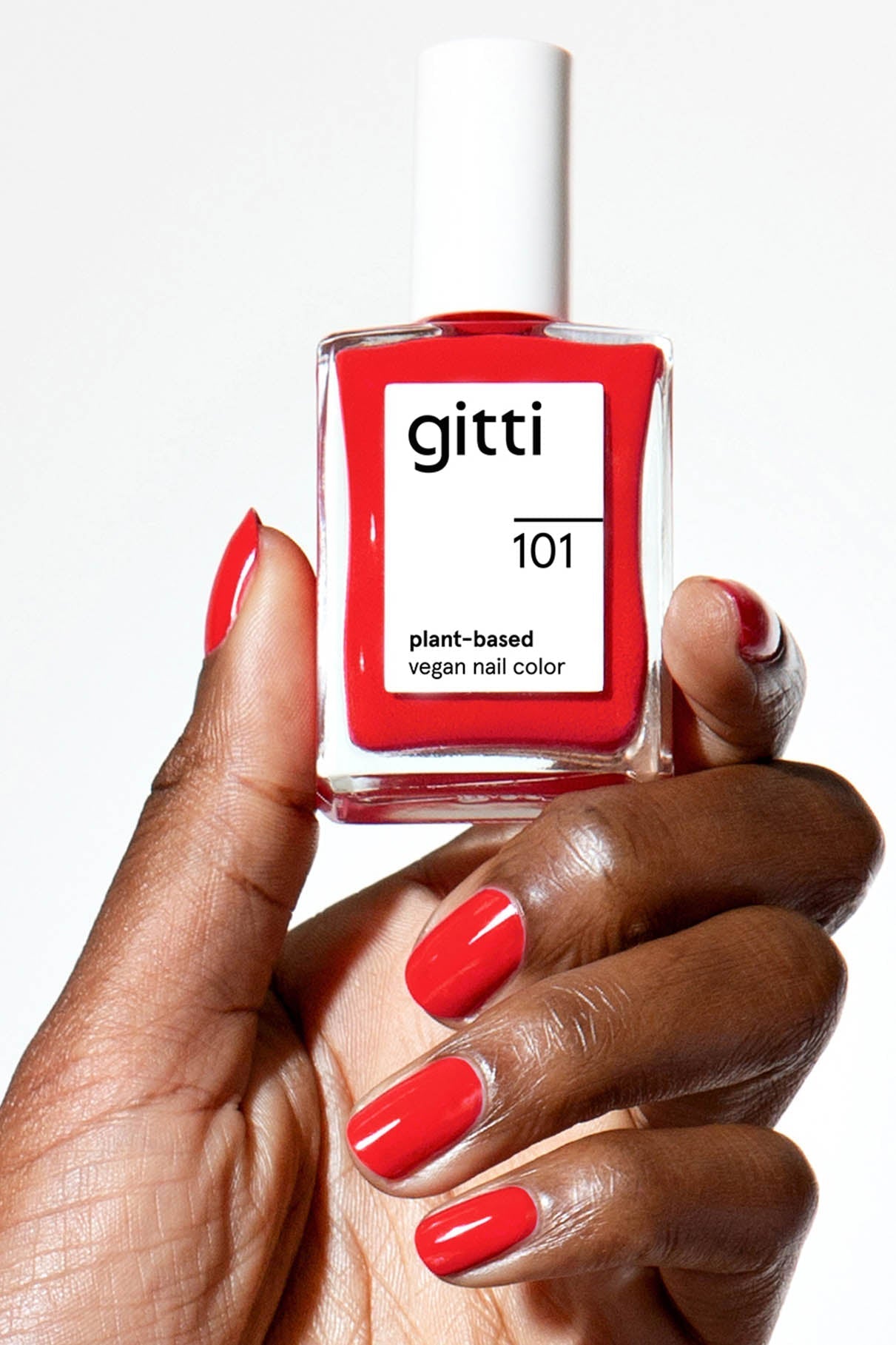 Eine Hand mit rot lackierten Nägeln hält eine Flasche der pflanzlichen veganen Nagelfarbe Nails + Lips in Sync.