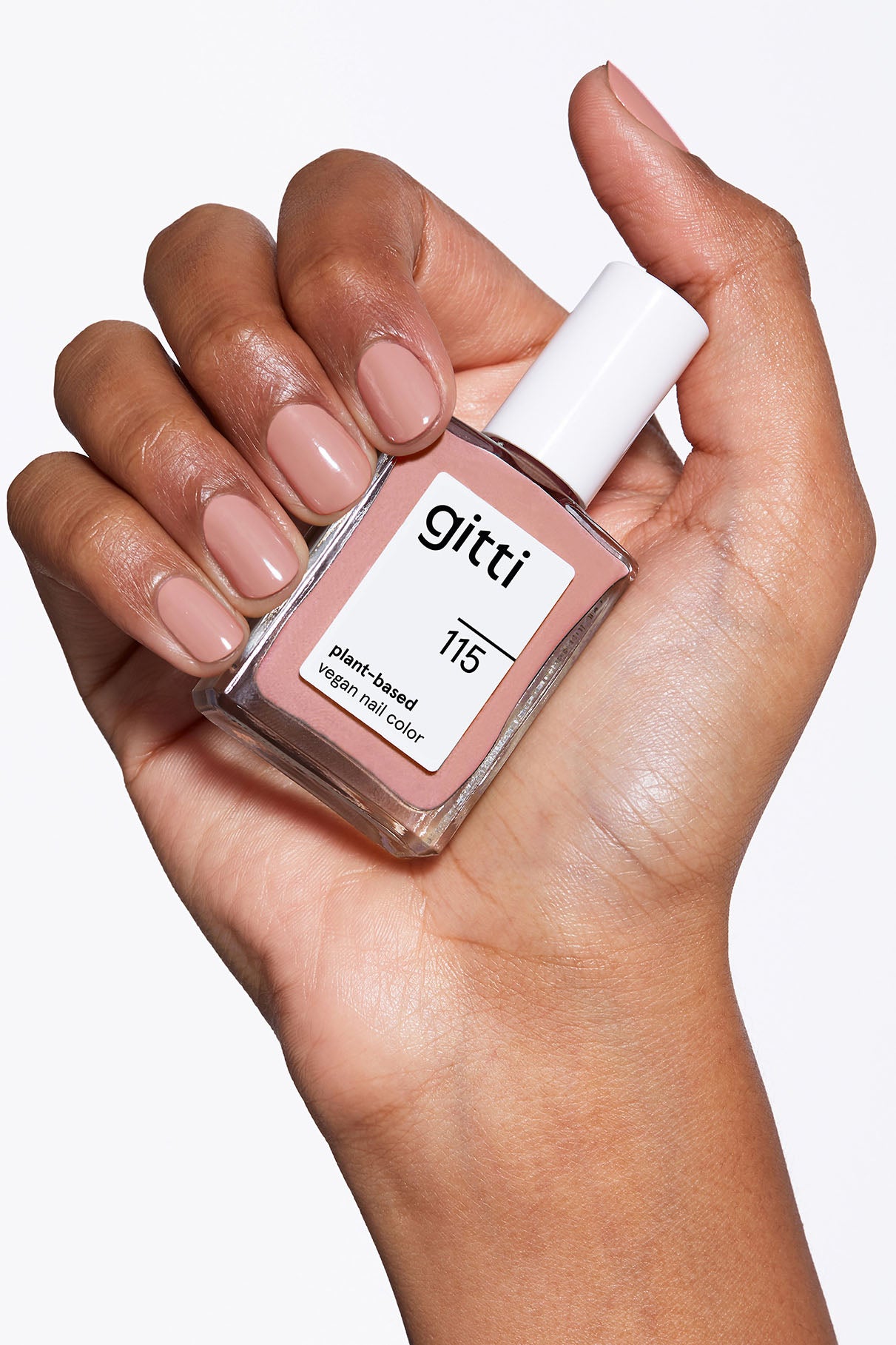 Eine Hand mit kurzen, sauber manikürten Nägeln, die in einem hellen Beige-Braun-Ton lackiert sind, hält ein Fläschchen mit gitti no. 115 vegane Nagelfarbe auf Pflanzenbasis.