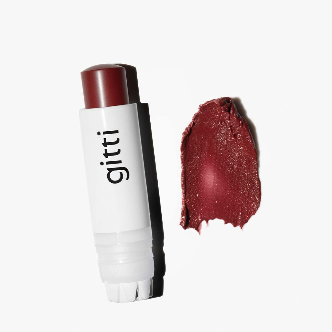Eine weiße Tube mit der Aufschrift gitti und ein dunkelroter Lippenstift aus dem Lash, Lip & Cheek Trio stehen neben einem passenden Farbabstrich und einem Visionist Lidschatten, alles auf weißem Hintergrund.