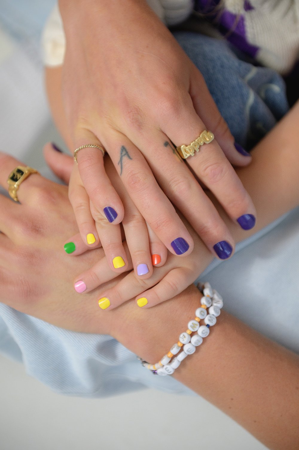 Zwei Hände mit buntem, kinderfreundlichem Nagellack aus dem Kids Duo ruhen aufeinander, zeigen Ringe und ein Perlenarmband - ideal für die Kleinen, die verspielte gitti kids Styles lieben.